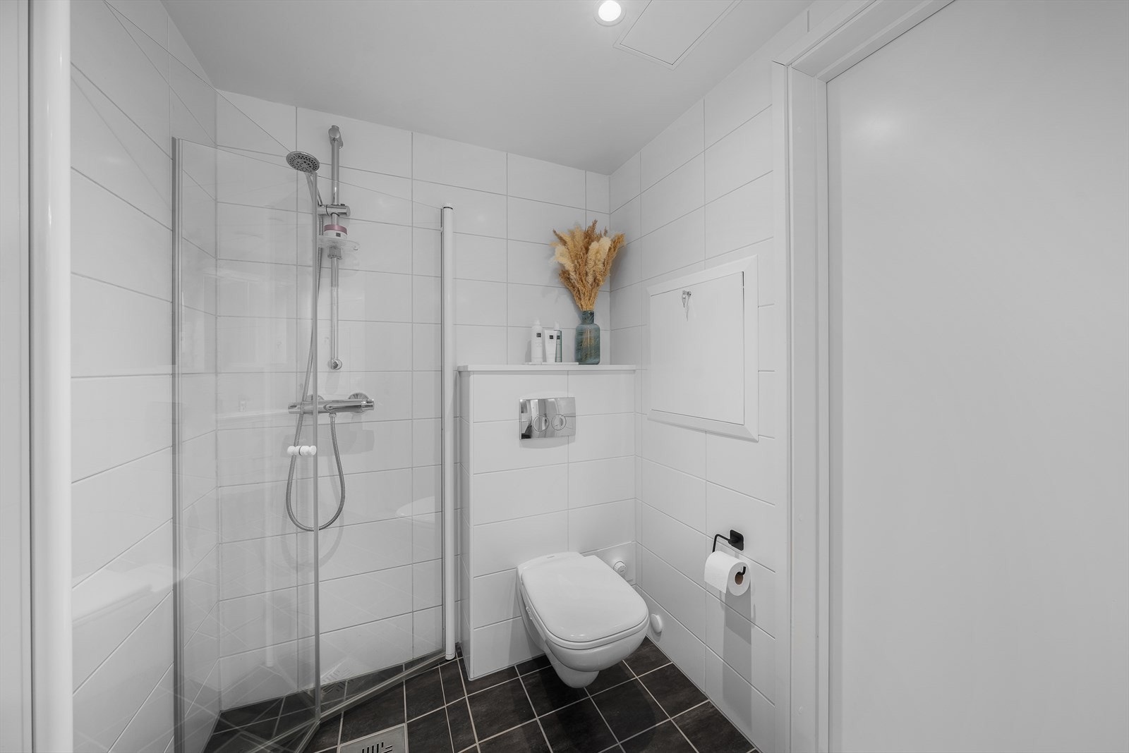 Badet er utstyrt med vegghengt toalett, servant med skuffer og dusjnisje med innfellbare glassdører. Galleribilde