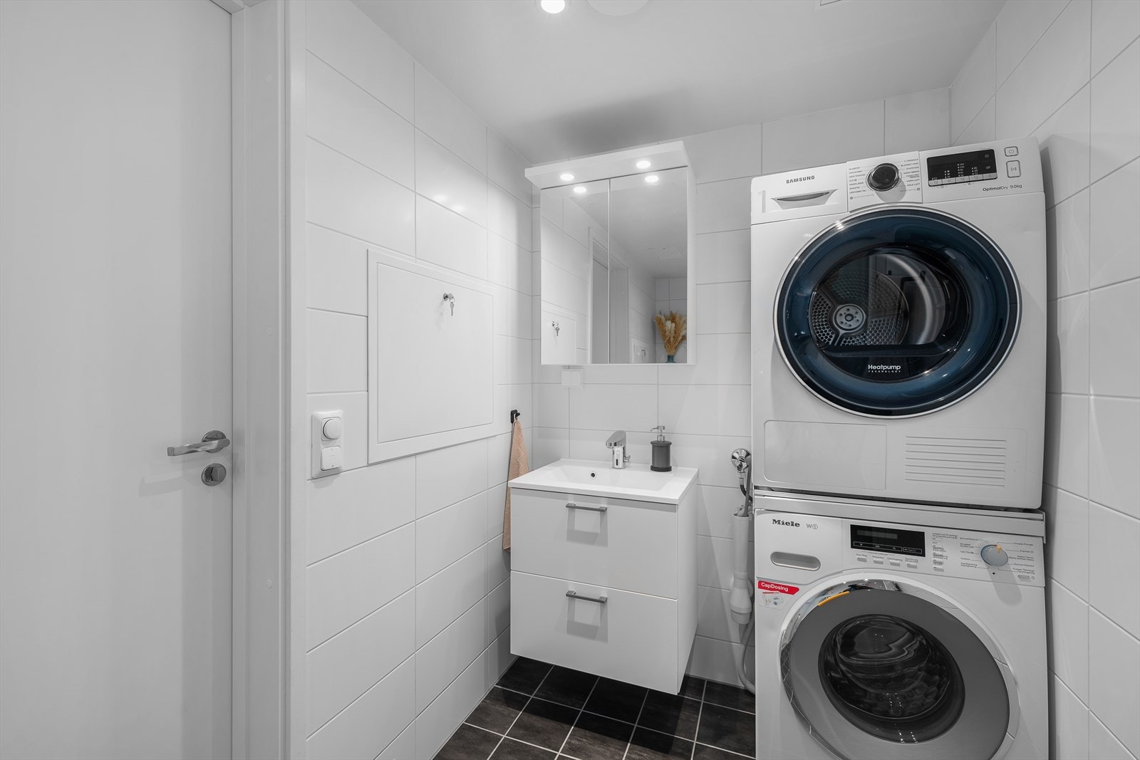 Pent flislagt baderom i tidløse fargetoner. Speilskap med belysning i overkant av servant og varme i gulv. Opplegg for vaskemaskin og plass til tørketrommel. Galleribilde