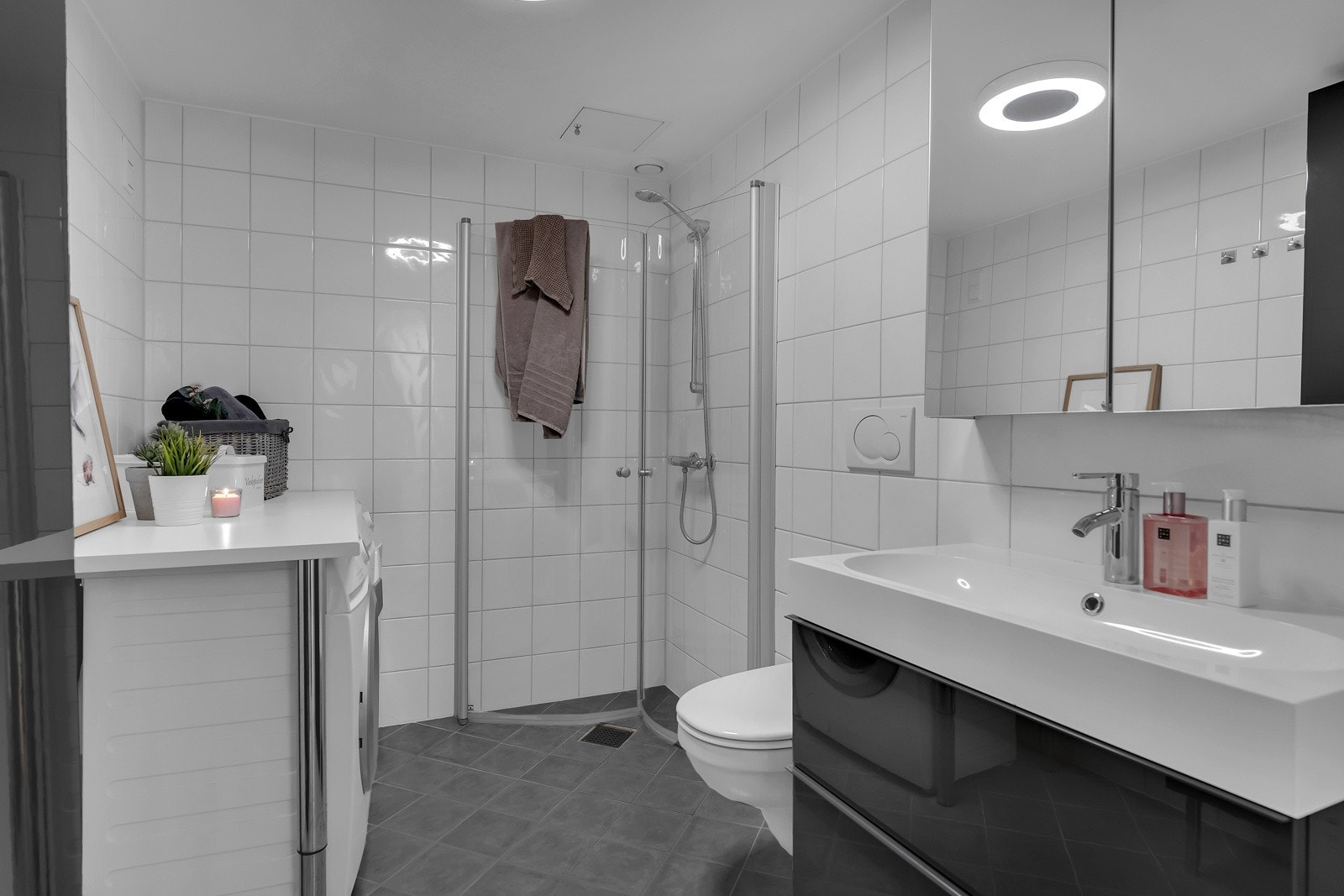 Badet fremstår tidløst med grå gulvfliser med varme, praktisk innredning og downlights i himling. Galleribilde