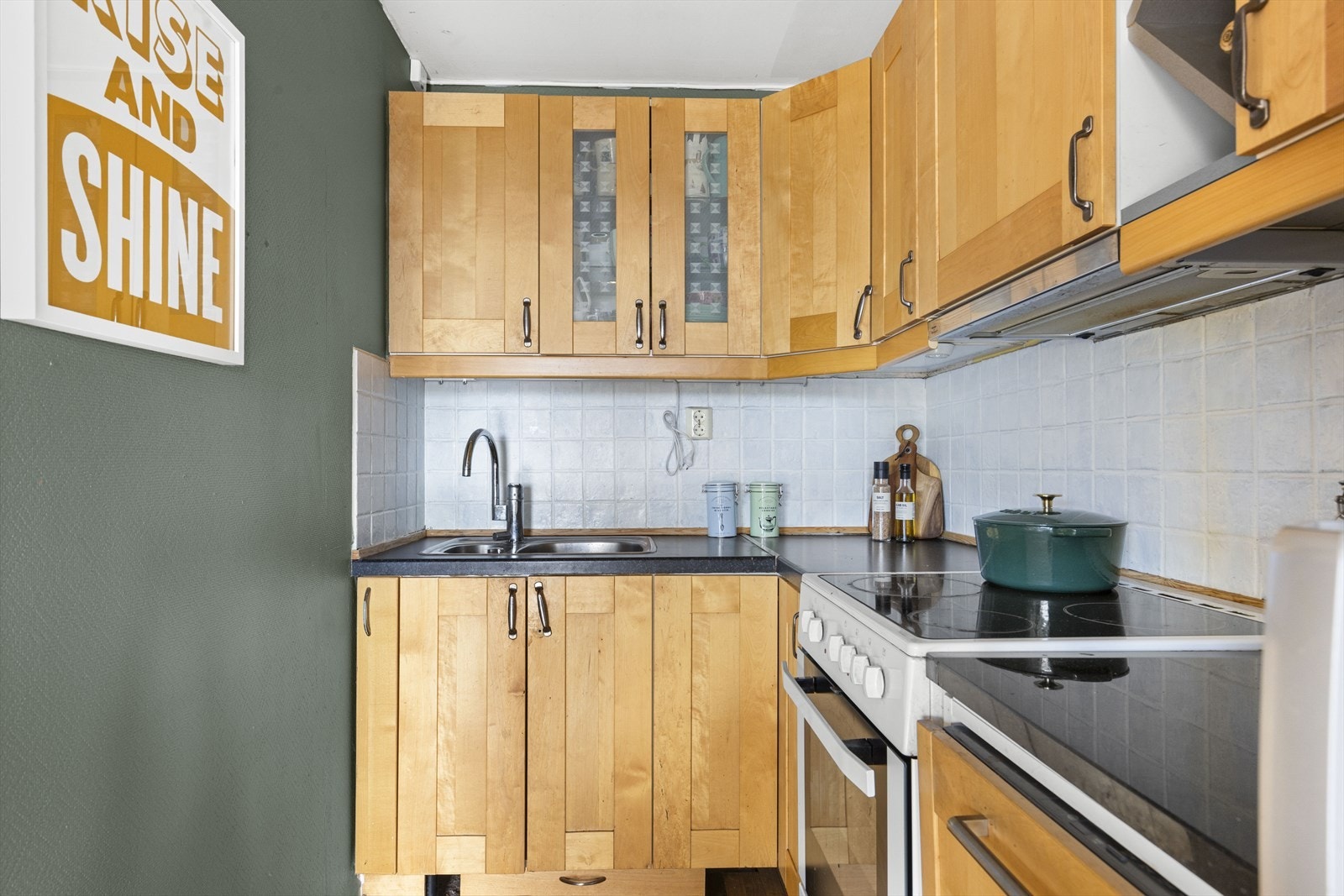 Kjøkkeninnredning med profilerte fronter. Laminat benkeplate med nedfelt vask-og skyllekum og benkeplate av stein. Fliser og belysning over kokeplass. Galleribilde