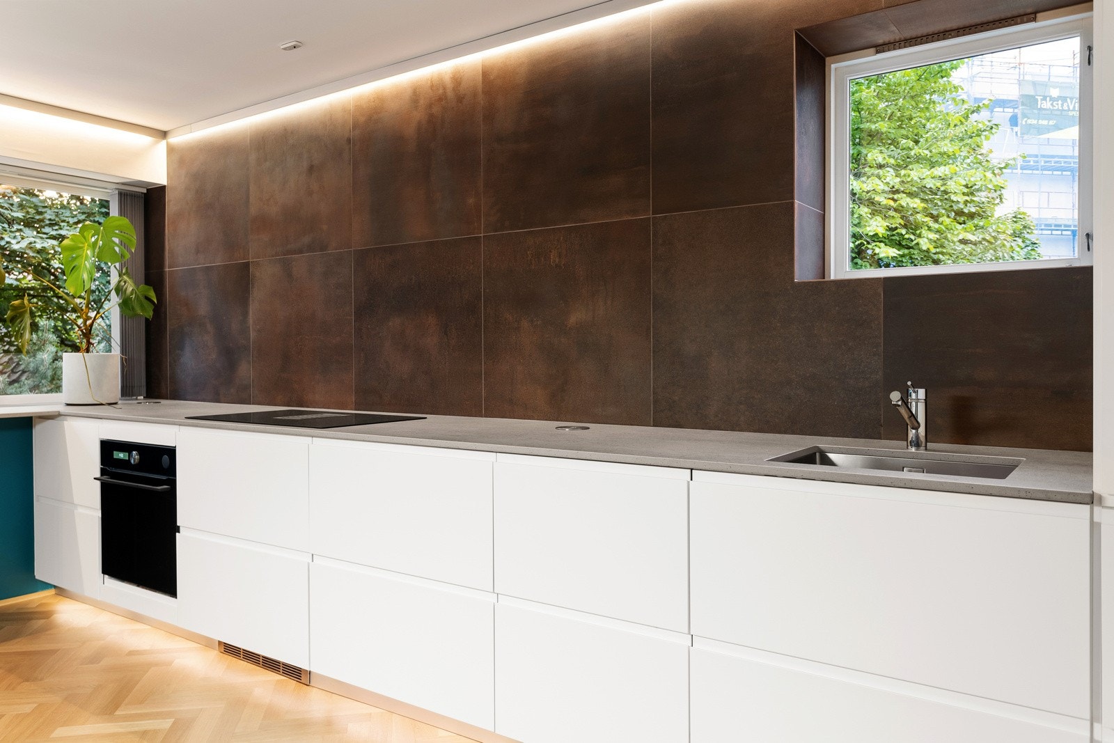 Kjøkkeninnredningen har glatte hvite fronter og benkeplate i kompositt med oppvaskkum i stål og stikkontakter Galleribilde