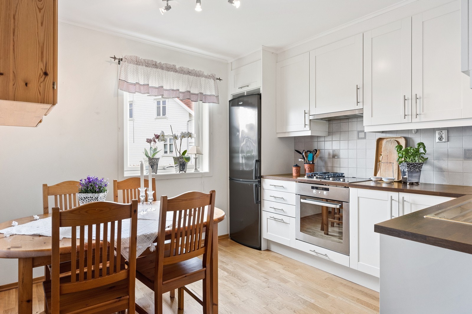 Kjøkken med hvite profilerte fronter, laminat benkeplate og integrert stekeovn og oppvaskmaskin. Platetopp med kombinert gass og induksjon. Galleribilde