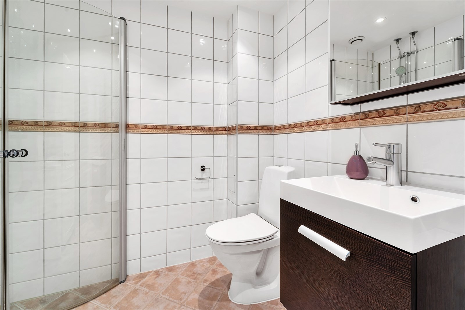 Velholdt bad med fliser på gulv og vegger, samt malt tak med downlights. Innredningen består av WC, servant med underskap, overskap med speilfronter, hengslede dusjdører, opplegg for vaskemaskin samt elektriske varmekabler i gulv. Vaskemaskinen medfølger. Galleribilde