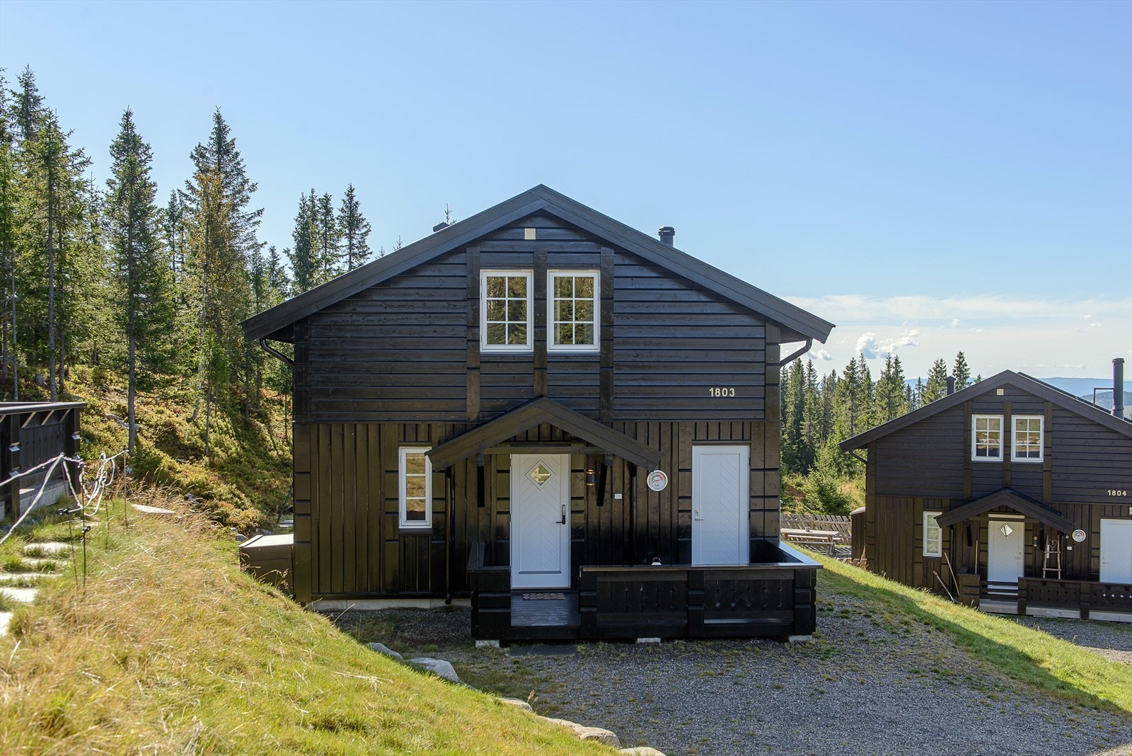 Gruset adkomst og parkeringsarealer. Hytta ligger i et veletablert område og i et tun som består av 8 hytter bygget ut på samme tiden. Galleribilde