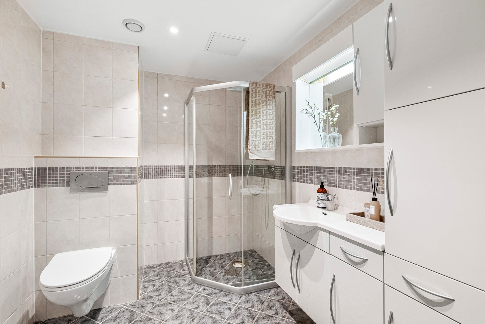 Badet er holdt i en tidløs stil med beige veggfliser og grå gulvfliser. Galleribilde