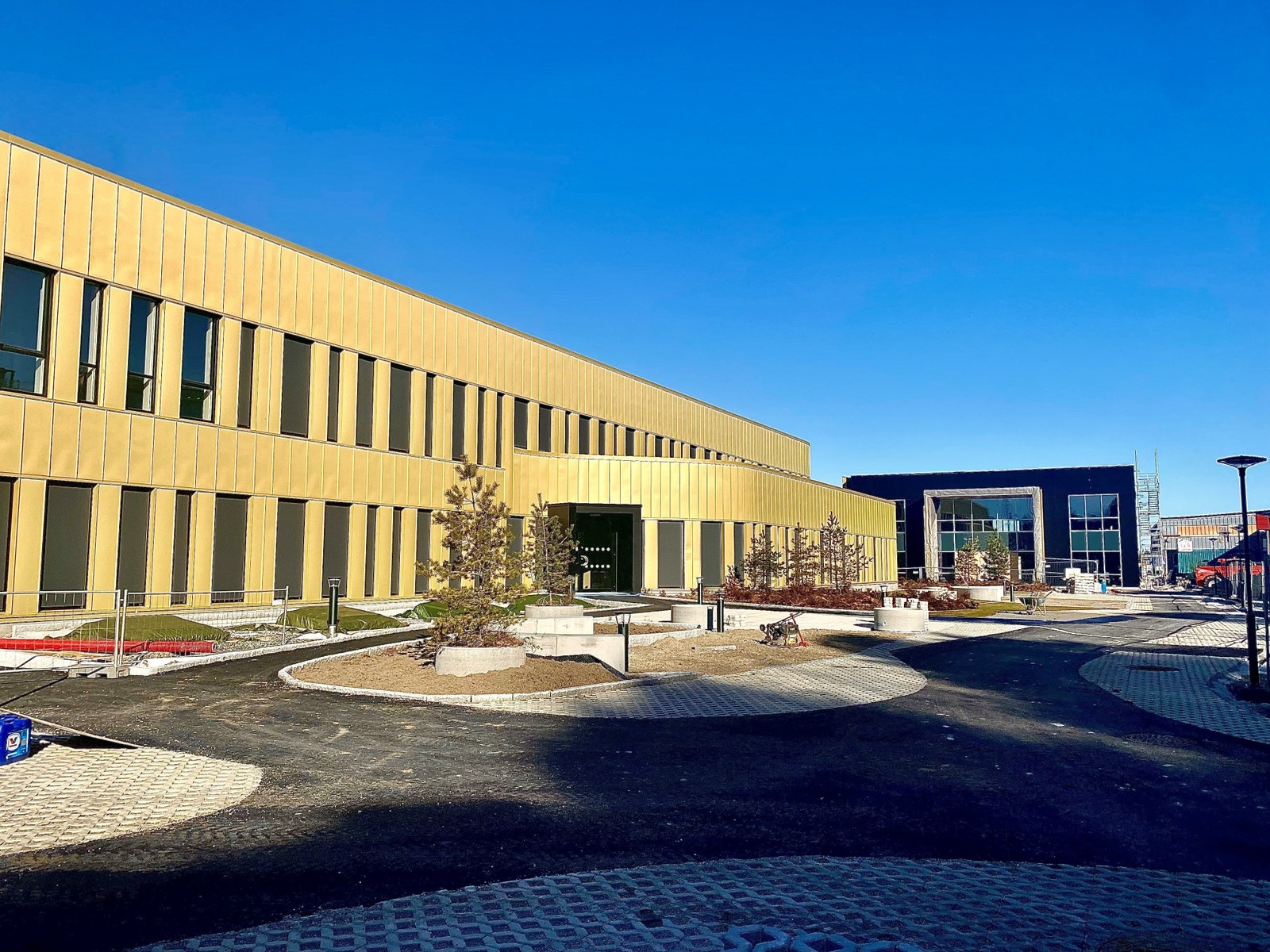 Byggene har en solfylte og lune uteområdet på begge sider. I bakgrunnen ser vi hovedinngangen til vårt effektive "Hybridbygg 1". Bygget er Breeam Serftifisert og har store vindusflater og parkering i underetasjen. Her er det plass til både handel, kontor Galleribilde