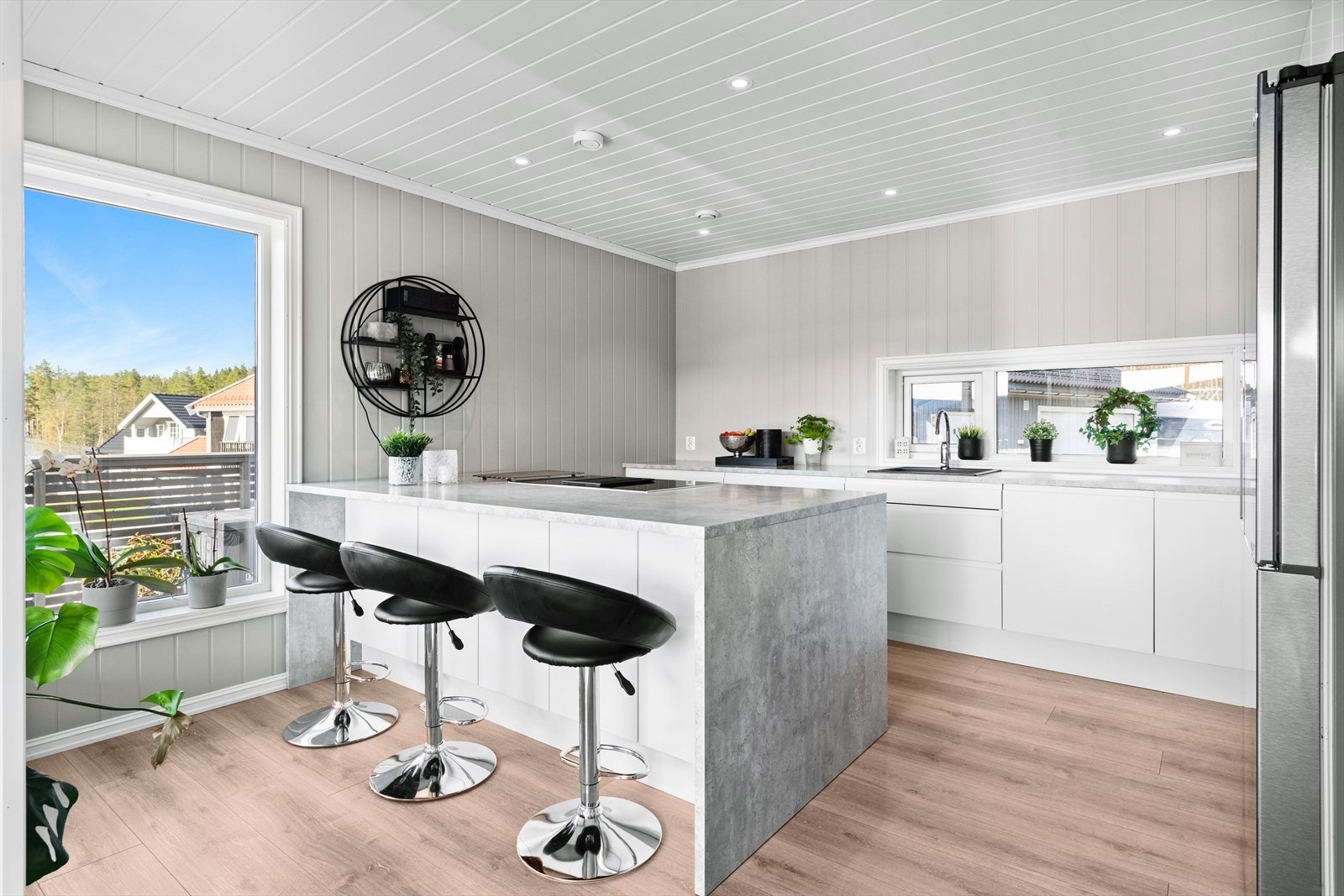 Lekker vinklet kjøkkeninnredning med øy og høyskap langs en vegg. Galleribilde