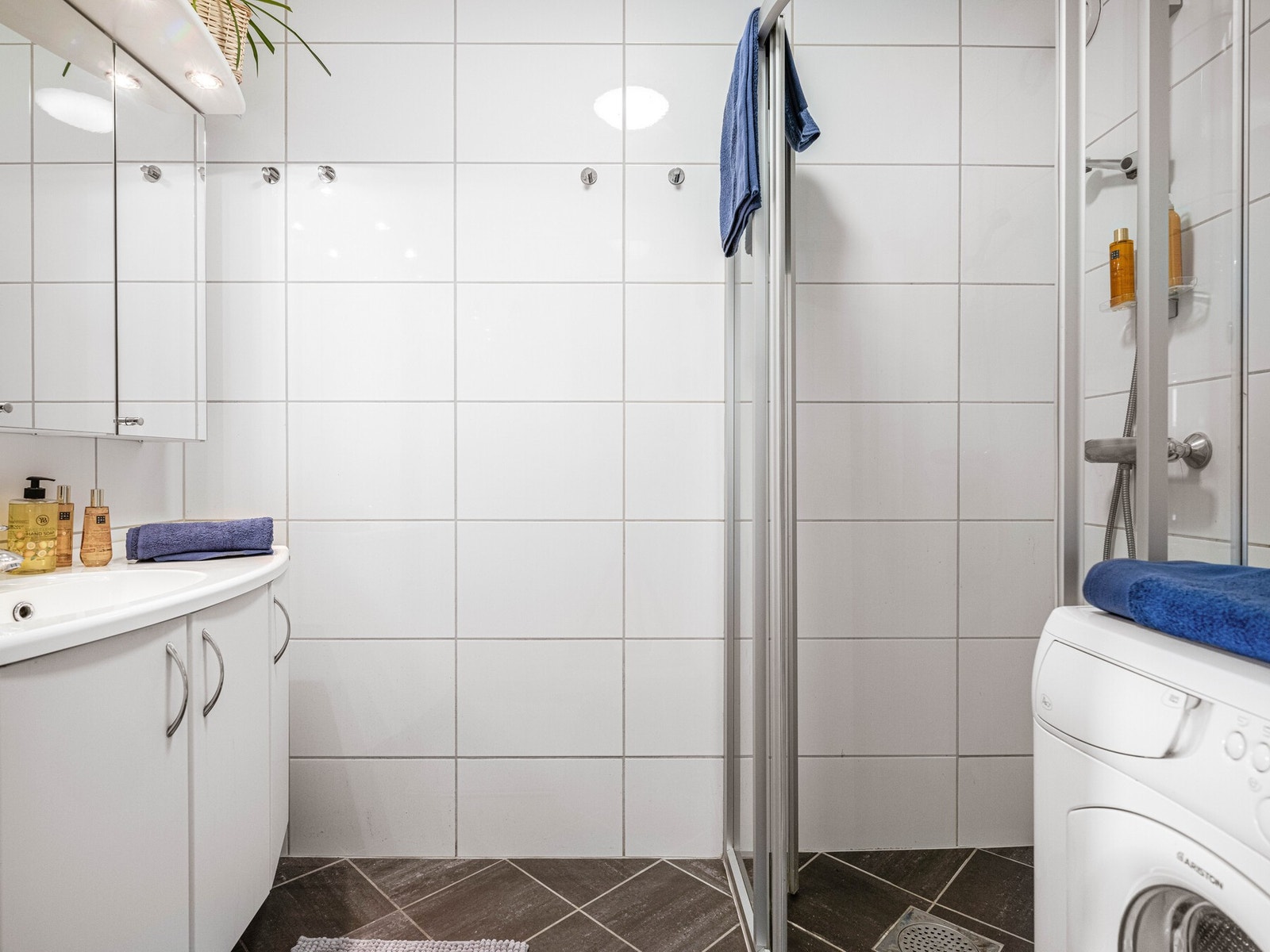 Flislagt bad med servantskap, dusjhjørne og kran og avløp til vaskemaskin. Galleribilde