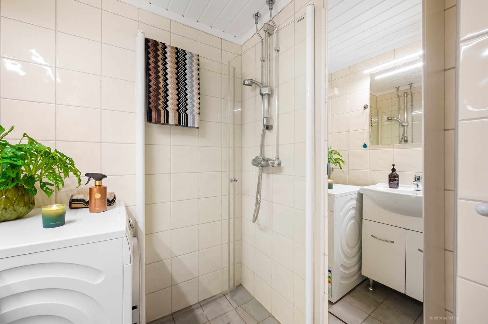 Badet er innredet med toalett, baderomsinnredning med servant, dusjhjørne med foldbare glassdører og opplegg til vaskemaskin. Galleribilde