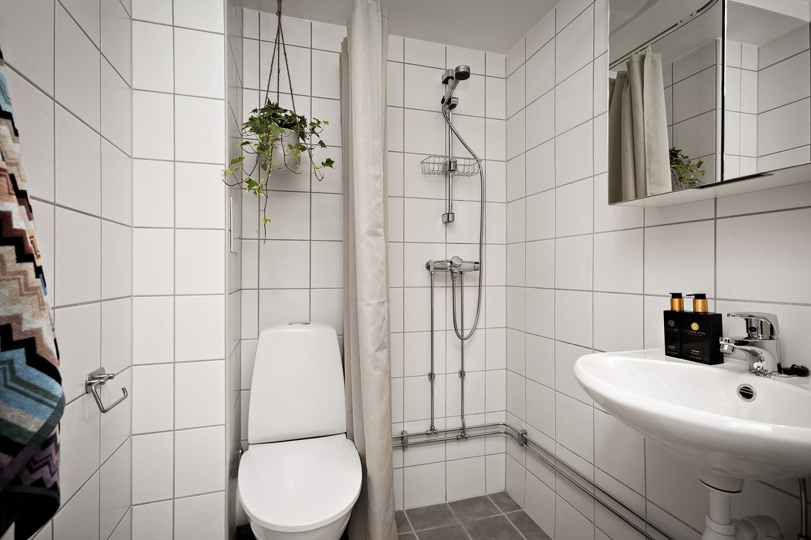 Innredningen på badet består av gulvstående toalett, servant med speilskap og dusjhjørne med forheng. Galleribilde