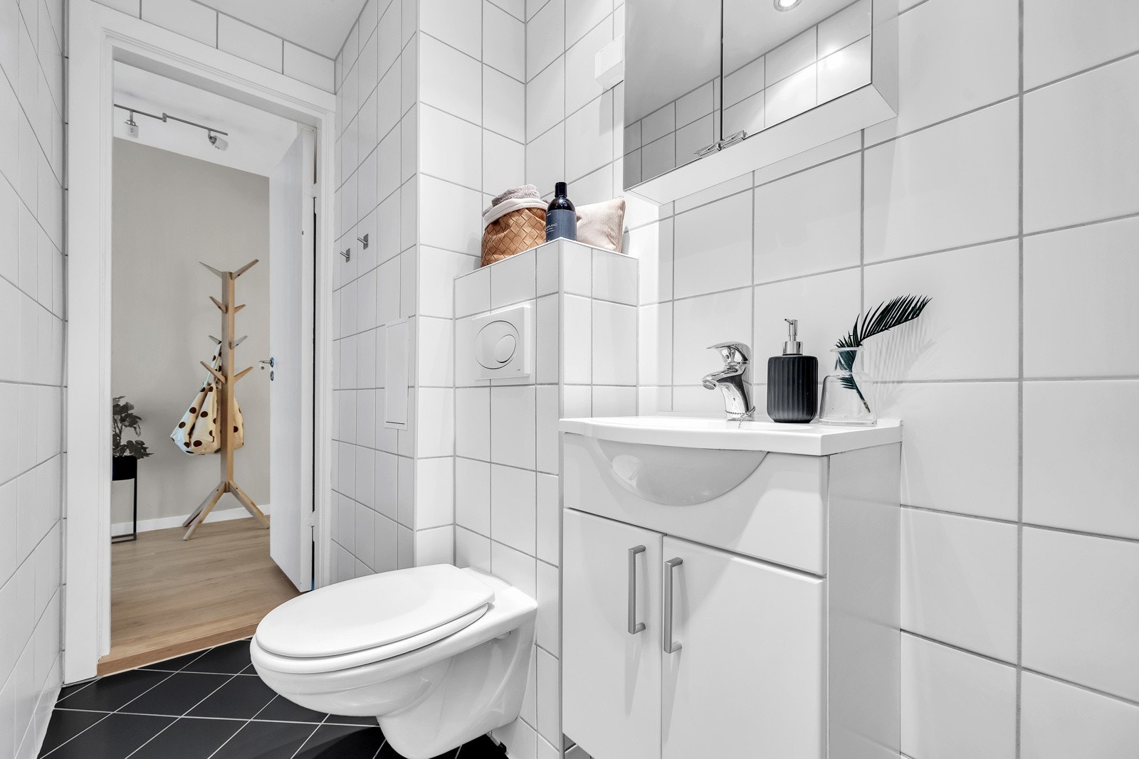 Et pent og tidløst baderom med mørke gulvfliser med varmekabler, hvite veggfliser og downlightsbelysning med dimmer. Galleribilde