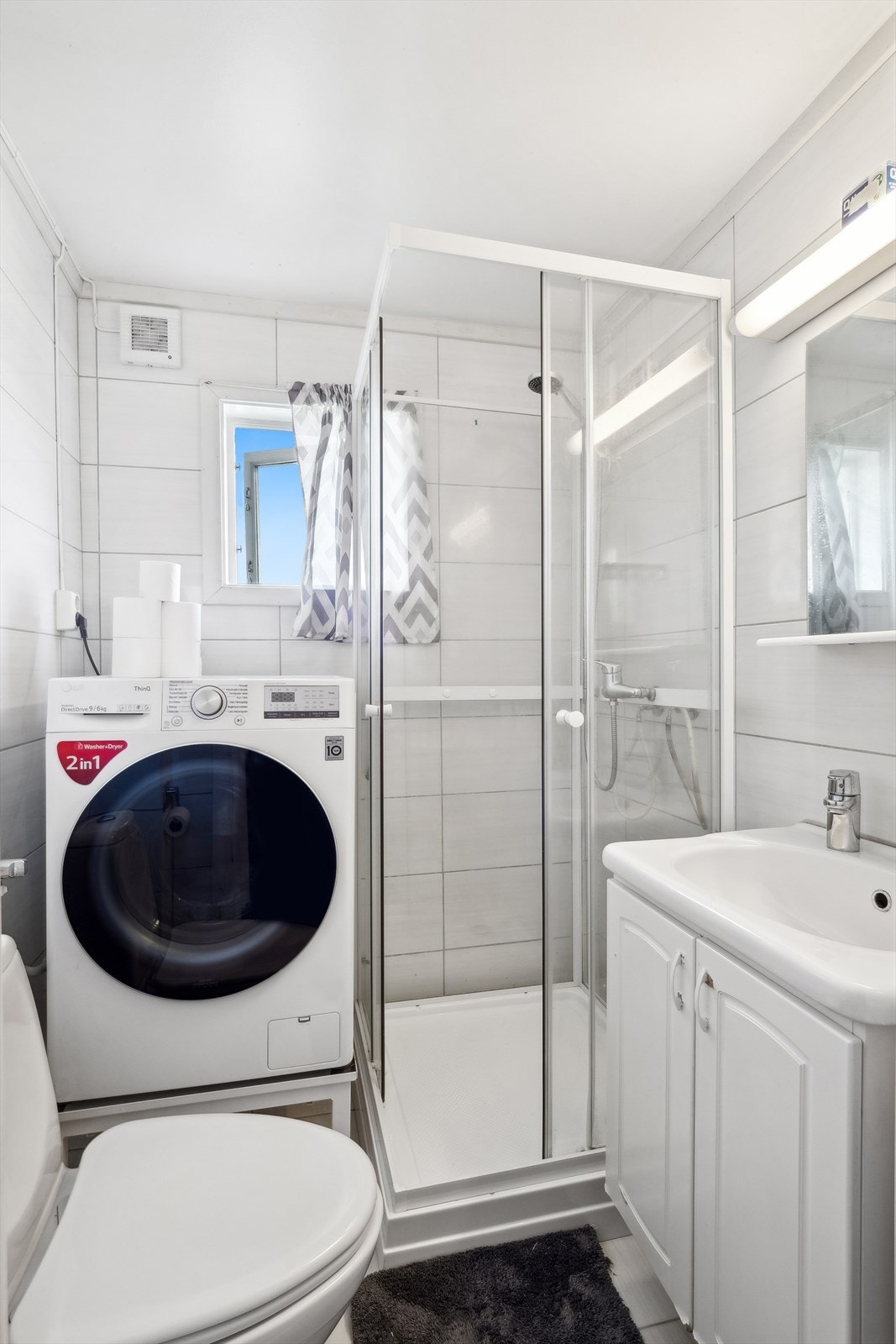 Flislagt baderom med malt himling. Badet er utstyrt med servant med underskap, speil med tilhørende belysning, dusjkabinett og gulvmontert toalett. Det er plass og opplegg til vaskemaskin. Galleribilde