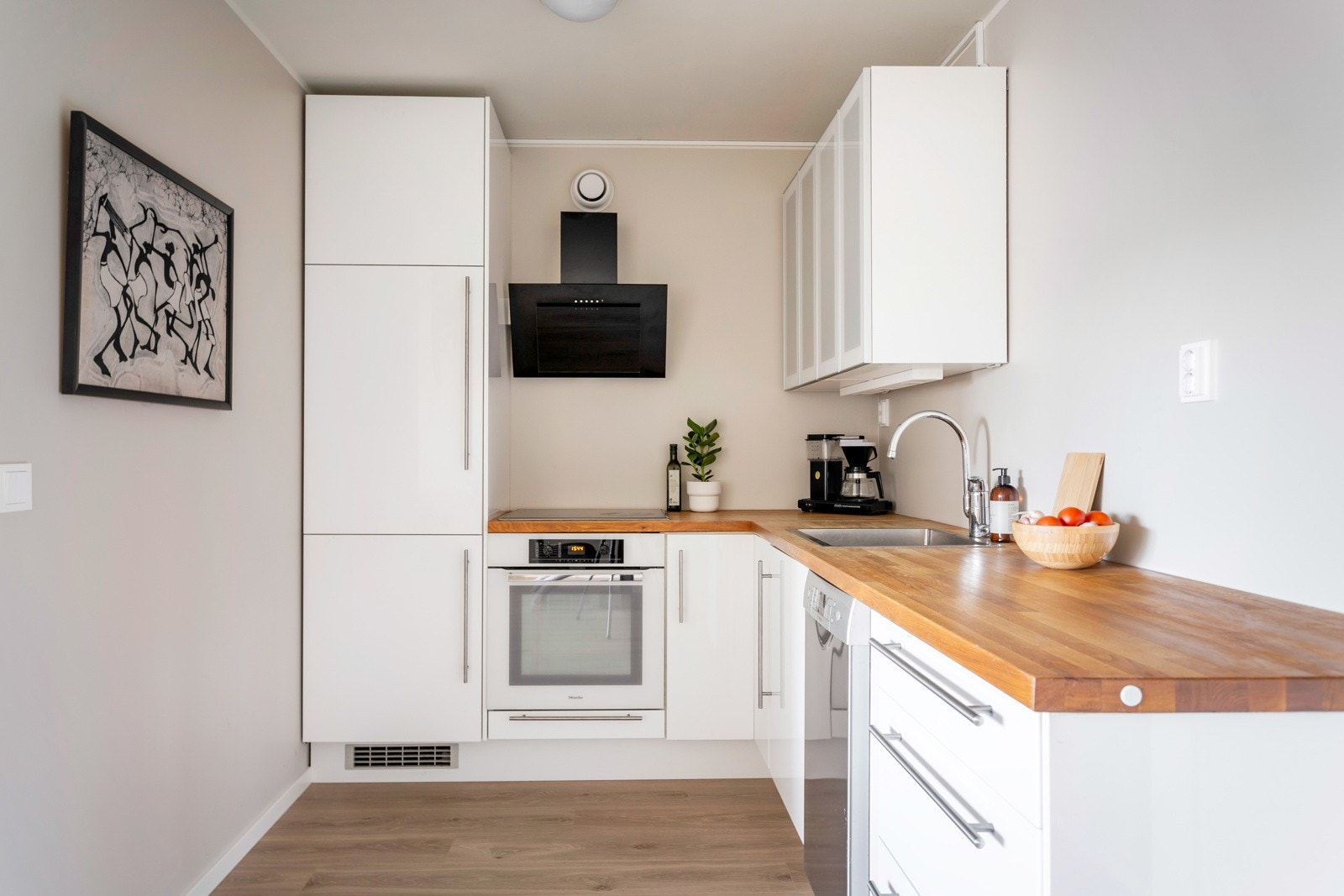 Kjøkkeninnredning med hvite glatte fronter og benkeplater av tre med nedfelt oppvaskkum i rudtfritt stål med ett-greps armatur. Galleribilde