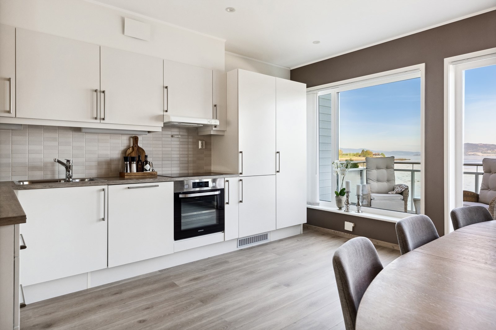 Kjøkkeninnredningen er fra HTH og har hvite, glatte fronter og en lys benkeplate med nedfelt oppvaskkum. Det er montert fliser mellom benk og overskap, og det er ventilator over kokesonen. Galleribilde