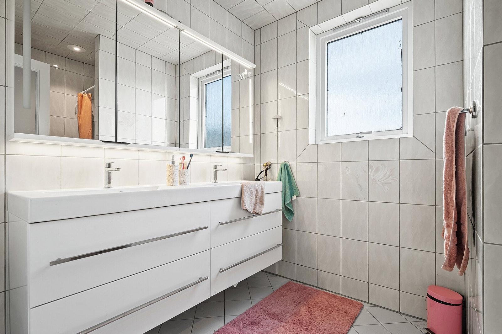 Flislagt bad med dusjhjørne og servant. Rett ved siden av er det vaskerom med toalett, opplegg for vaskemaskin og servant Galleribilde