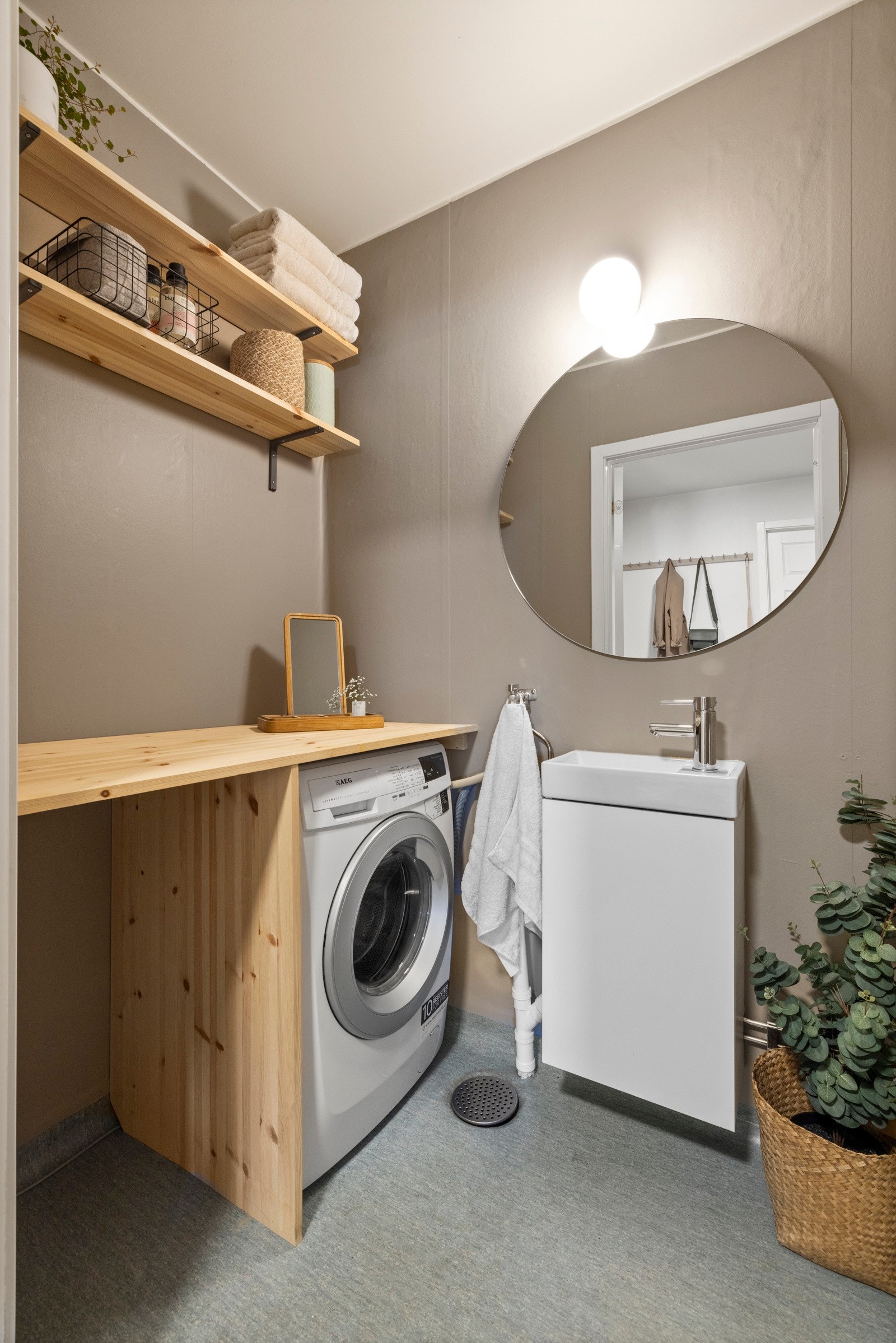 WC-rommet har gulvbelegg og opplegg for vaskemaskin under hendig benk og åpne hyller Galleribilde