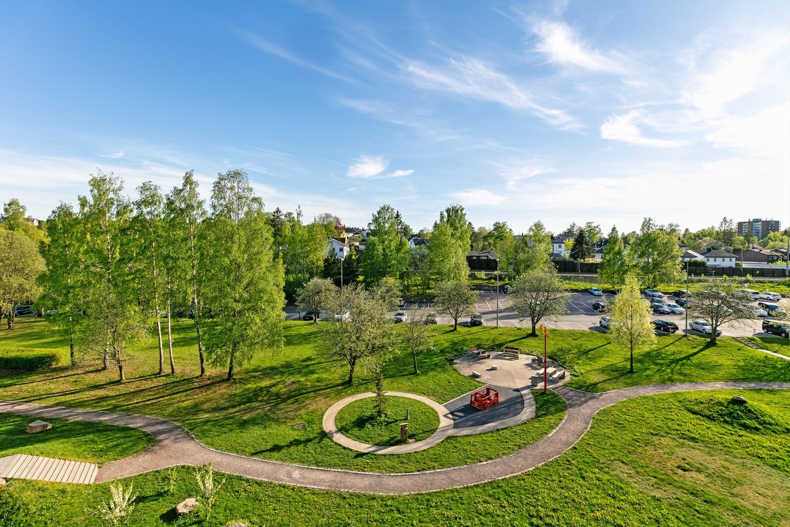 Stort fellesareal opparbeidet med asfalterte adkomstveier/plasser, gressplen, beplantning, trær, lekeapparater, parkeringsarealer m.m. Galleribilde