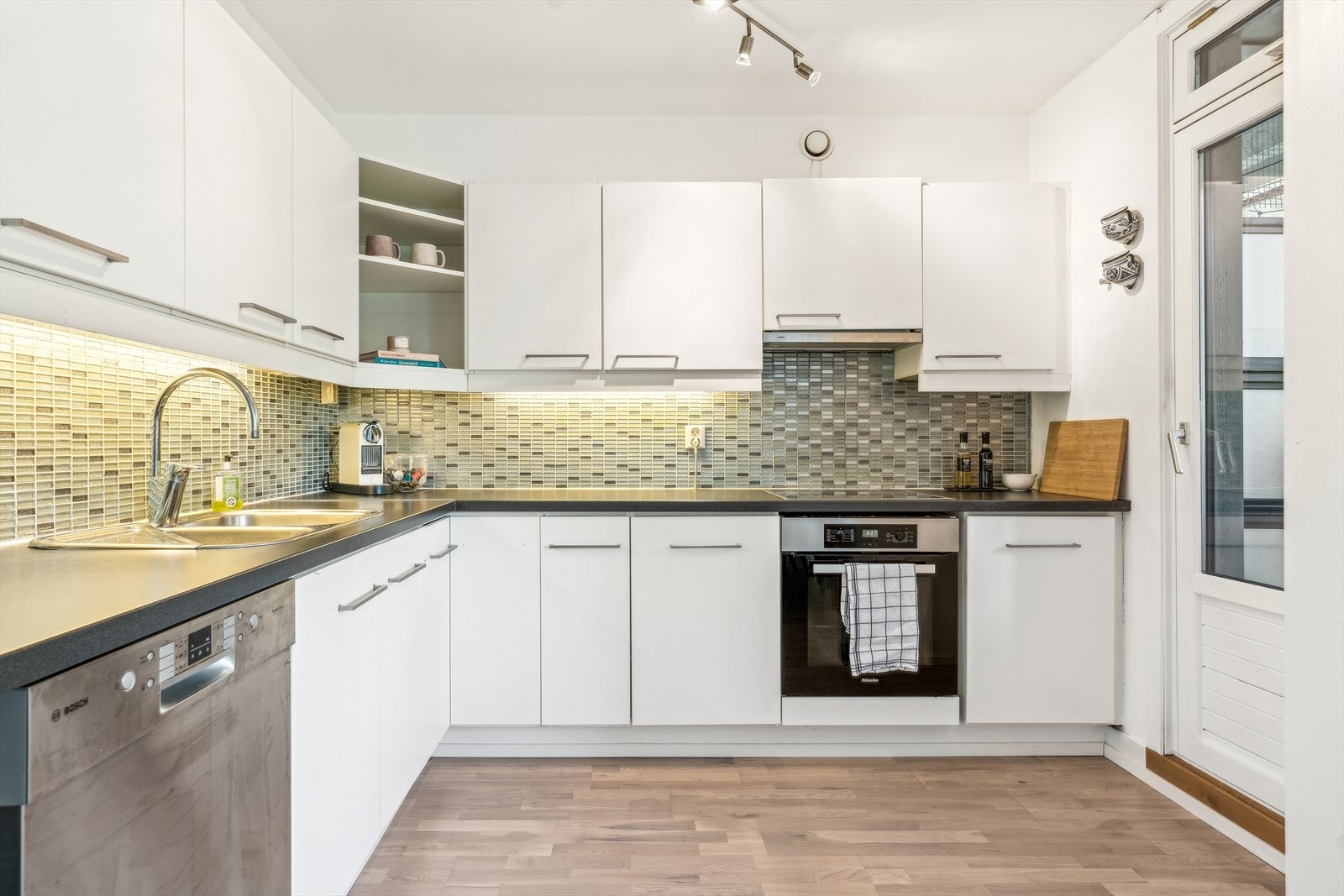 Kjøkkeninnredningen har hvite glatte fronter og sort laminert benkeplate, og ble oppgradert i 2010. Over kjøkkenbenken prydes veggene av vakre mosaikkfliser, mens benkebelysning under overskapene sørger for et funksjonelt og stemningsfullt kjøkkenmiljø. Galleribilde