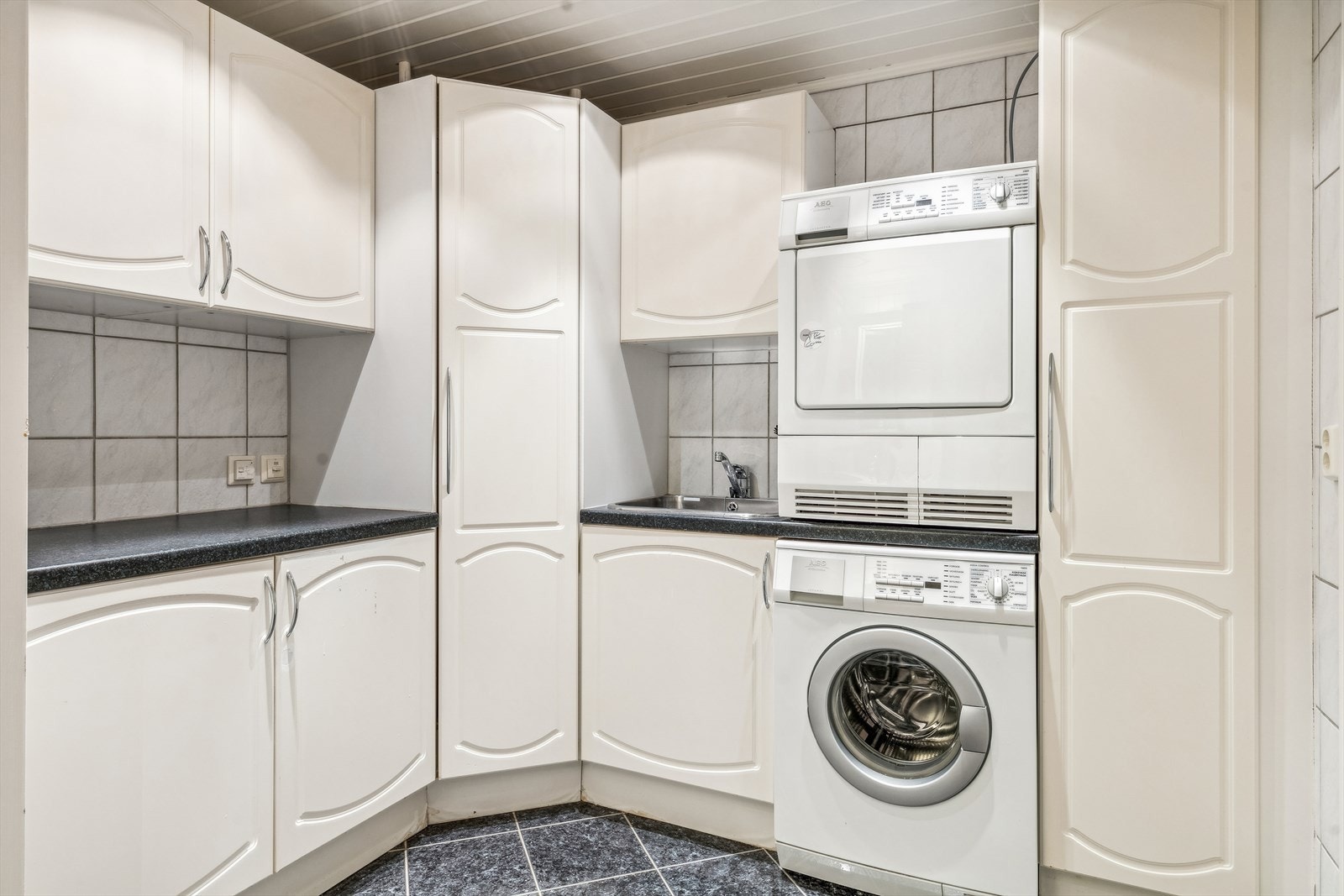 Badet er også innredet med en vaskeromsinnredning med hvite profilerte fronter, laminert benkeplate, skyllekum i stål, blandebatteri, samt opplegg og plass for vaskemaskin og tørketrommel. Galleribilde