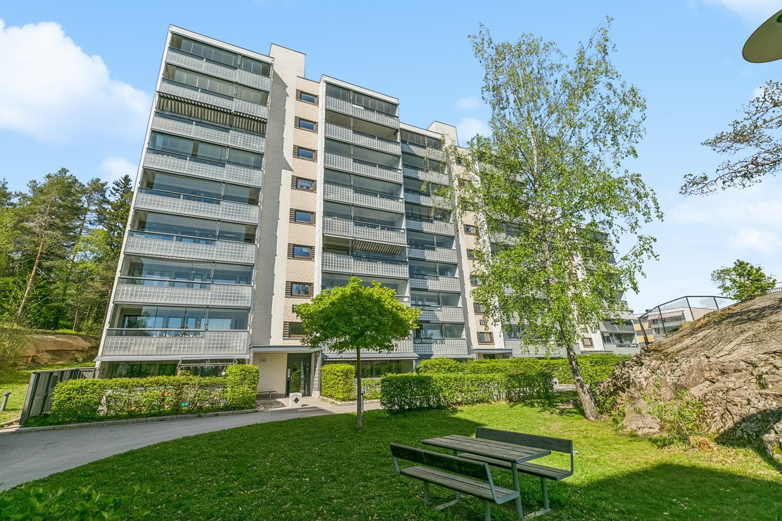 Pent opparbeidet fellesareal med asfalterte adkomstveier, gressplen, beplantning, sittegrupper og lekeapparater. Galleribilde