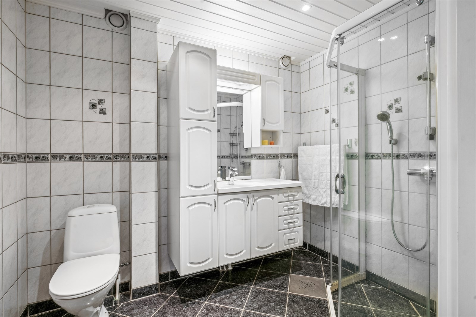 Leiligheten har et stort bad med flislagte gulv og vegger, og det er varmekabler i gulvet. Himling med malt trepanel og downlights. Galleribilde