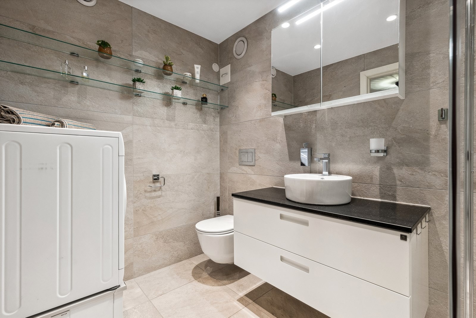 Badet er utstyrt med speilskap, servant med skuffeseksjon og opplegg for vaskemaskin Galleribilde