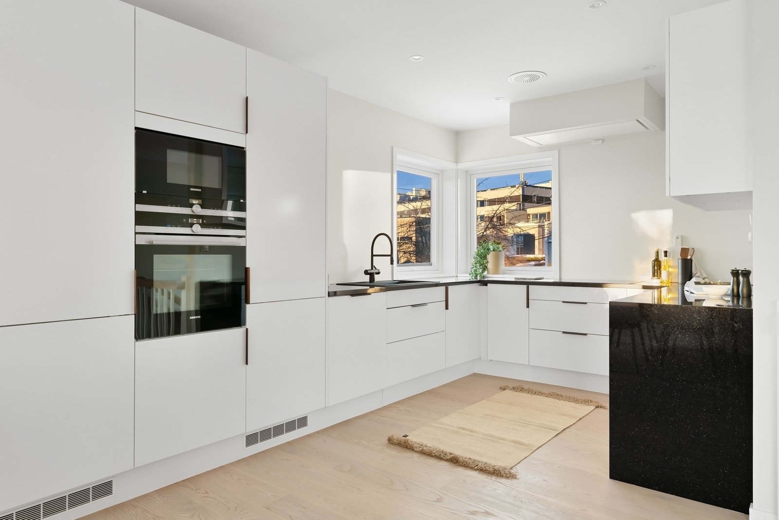 Innholdsrikt og stilrent kjøkken med integrerte hvitevarer fra Siemens, herunder induksjonstopp med ventilator i overkant, stekeovn, kombiovn, kjøl/fryseskap og oppvaskmaskin. Galleribilde