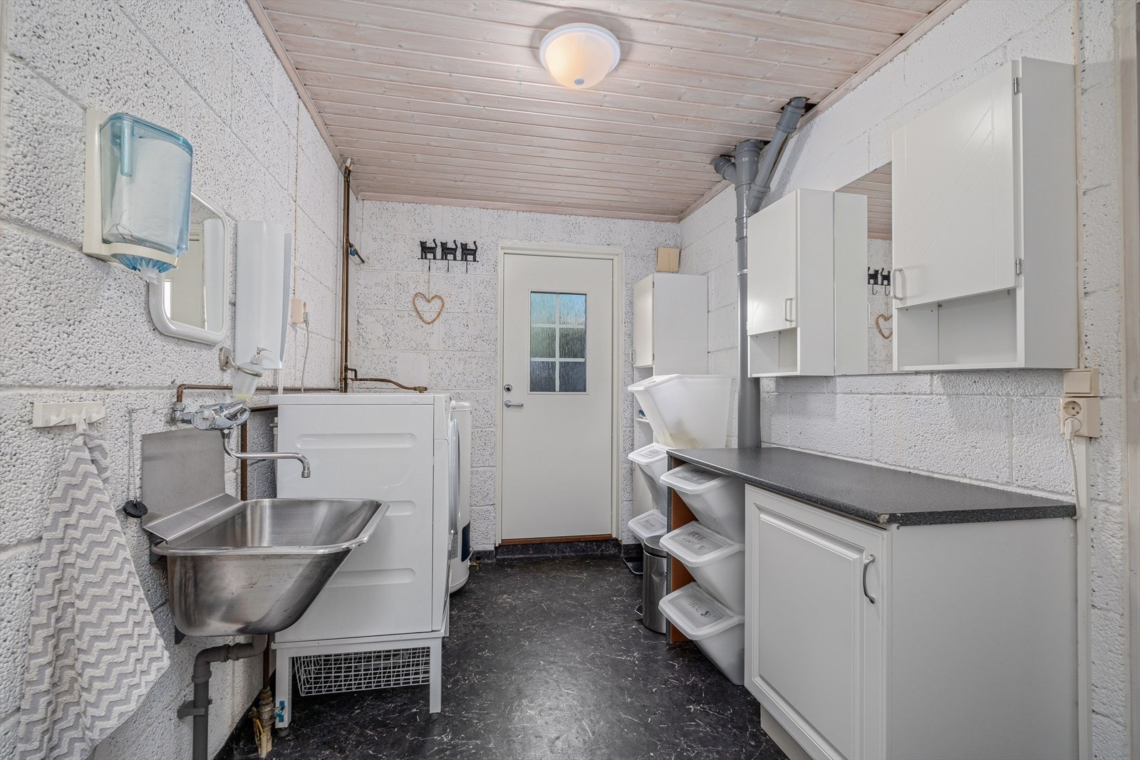 Vaskerom med gulvbelegg og varmekabler på gulv, malte lettklinkerblokker på vegg og beiset panel i himling. Innredet med benkeskap og overskap. Stålkum og opplegg for vaskemaskin og tørketrommel. Galleribilde