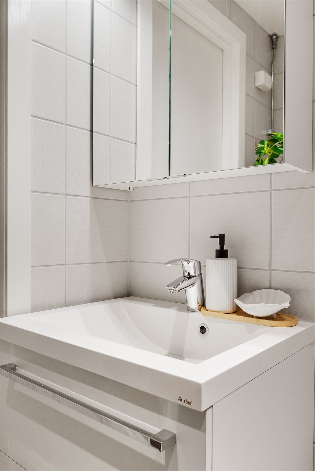 Glatt baderomsinnredning med heldekkende servant nedfeldt i underskap, speilskap m/lys, veggmontert toalett, dusjhjørne m/glassdører og opplegg for vaskemaskin. Galleribilde