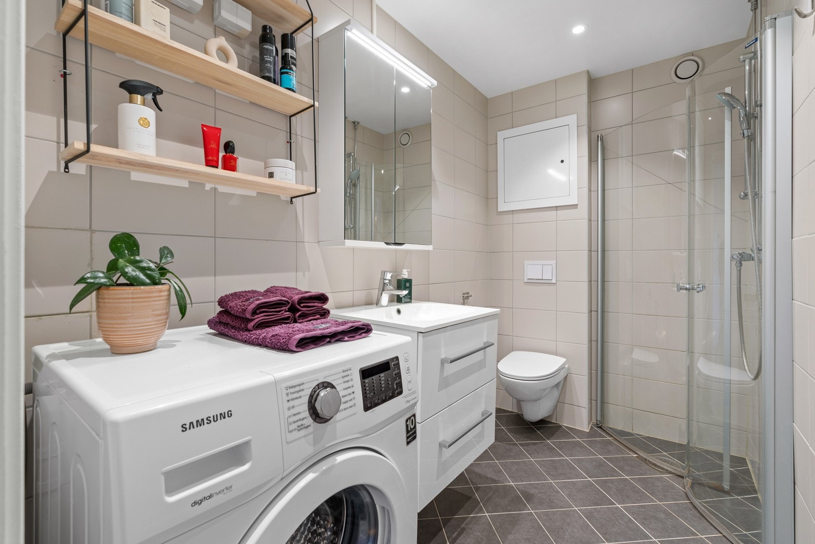 Innredning består av et veggmontert toalett og et dusjhjørne med innfellbare glassdører. Rommet gulvvarme og hvitmalt himling med downlights. Galleribilde