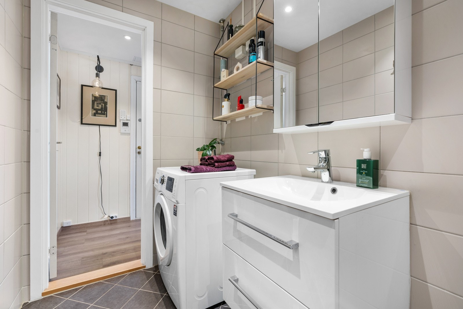 Ellers er det en heldekkende servant på hvit skuffeseksjon, speilskap med belysning og opplegg for vaskemaskin. Galleribilde