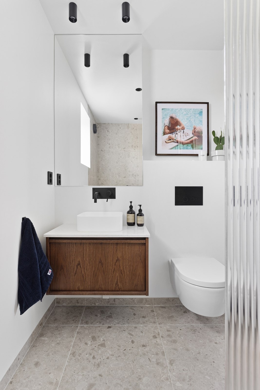 Badet er utstyrt med vegghengt wc, "skål" servant med snekkerbygget innredning/skuff under og dusj i hjørne med glassvegg. Armaturene er fint integrerte. Galleribilde