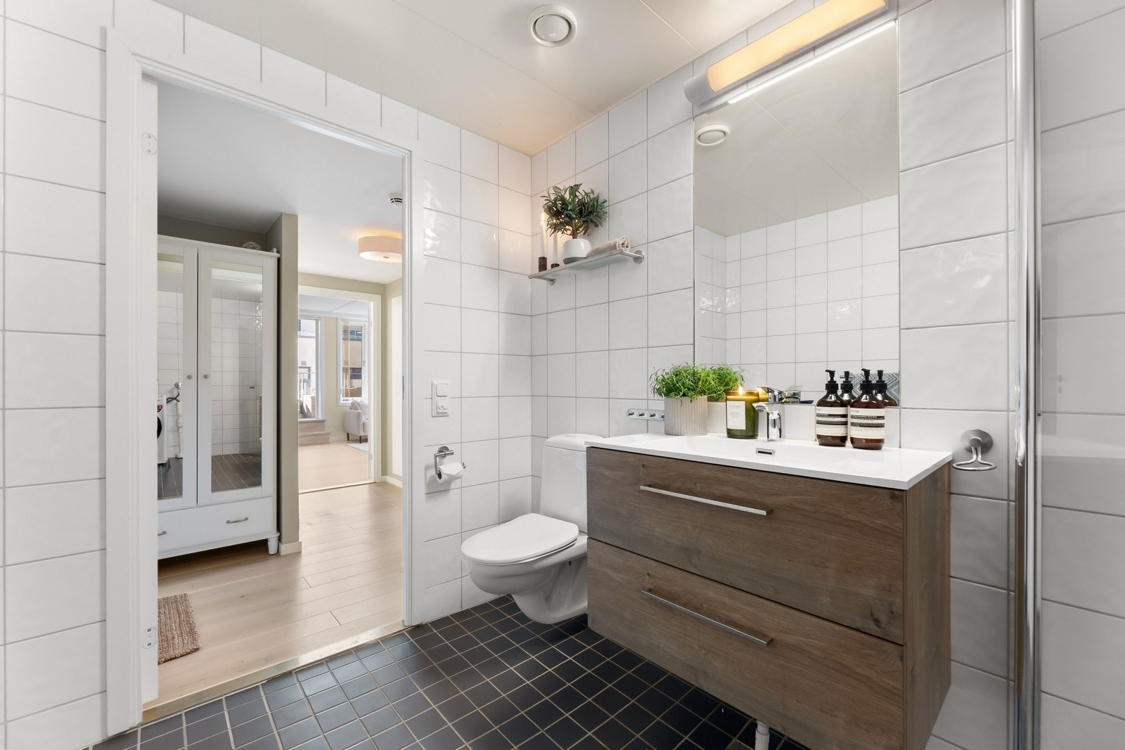 Pent flislagt baderom med gulvvarme, speil med innebygd belysning, nedfelt servant i skapinnredning, veggmontert toalett og dusjnisje. Galleribilde