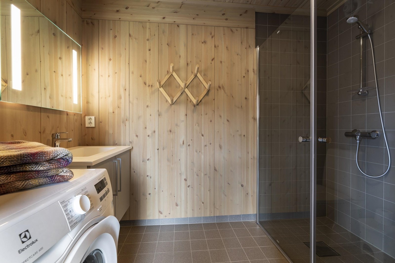 Badet har flislagt gulv og inneholder dusjkabinett, servant med underskap, wc og opplegg til vaskemaskin. Galleribilde