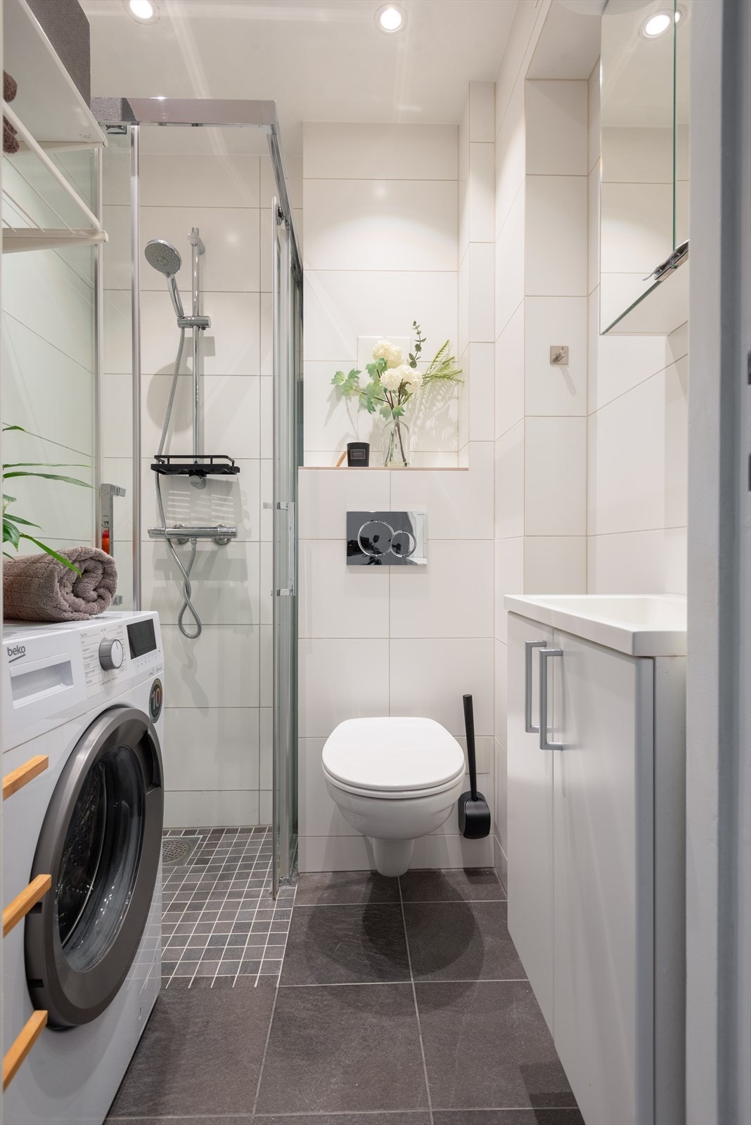 Delikat flislagt bad med gulvvarme og downlights. Servantskap med glatte fronter, veggmontert wc og speilskap med spotter Galleribilde