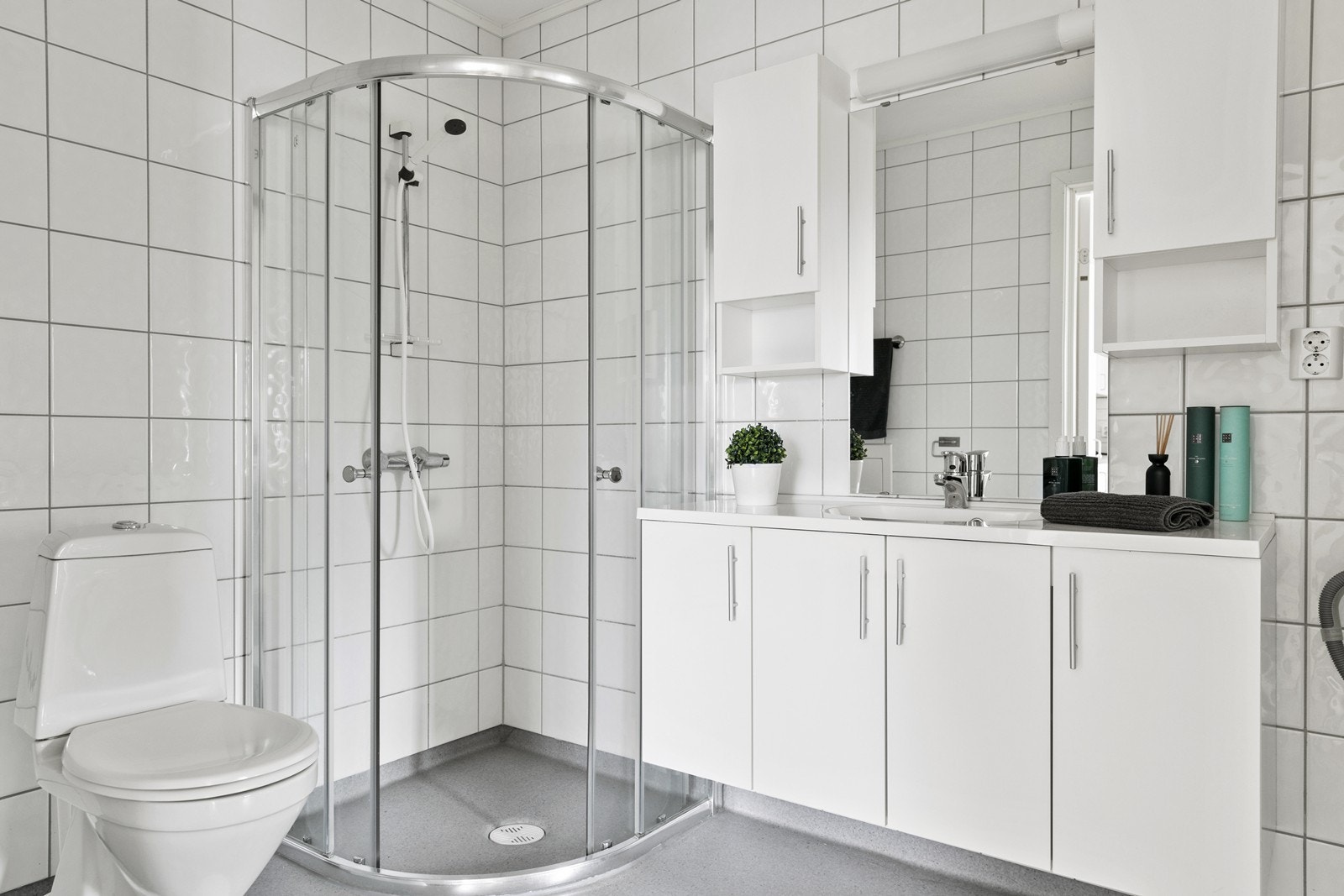Badet er utstyrt med klassisk baderomsinnredning med heldekkende servant, og speil mellom overskap. I tillegg er det dusjhjørne og gulvmontert wc Galleribilde