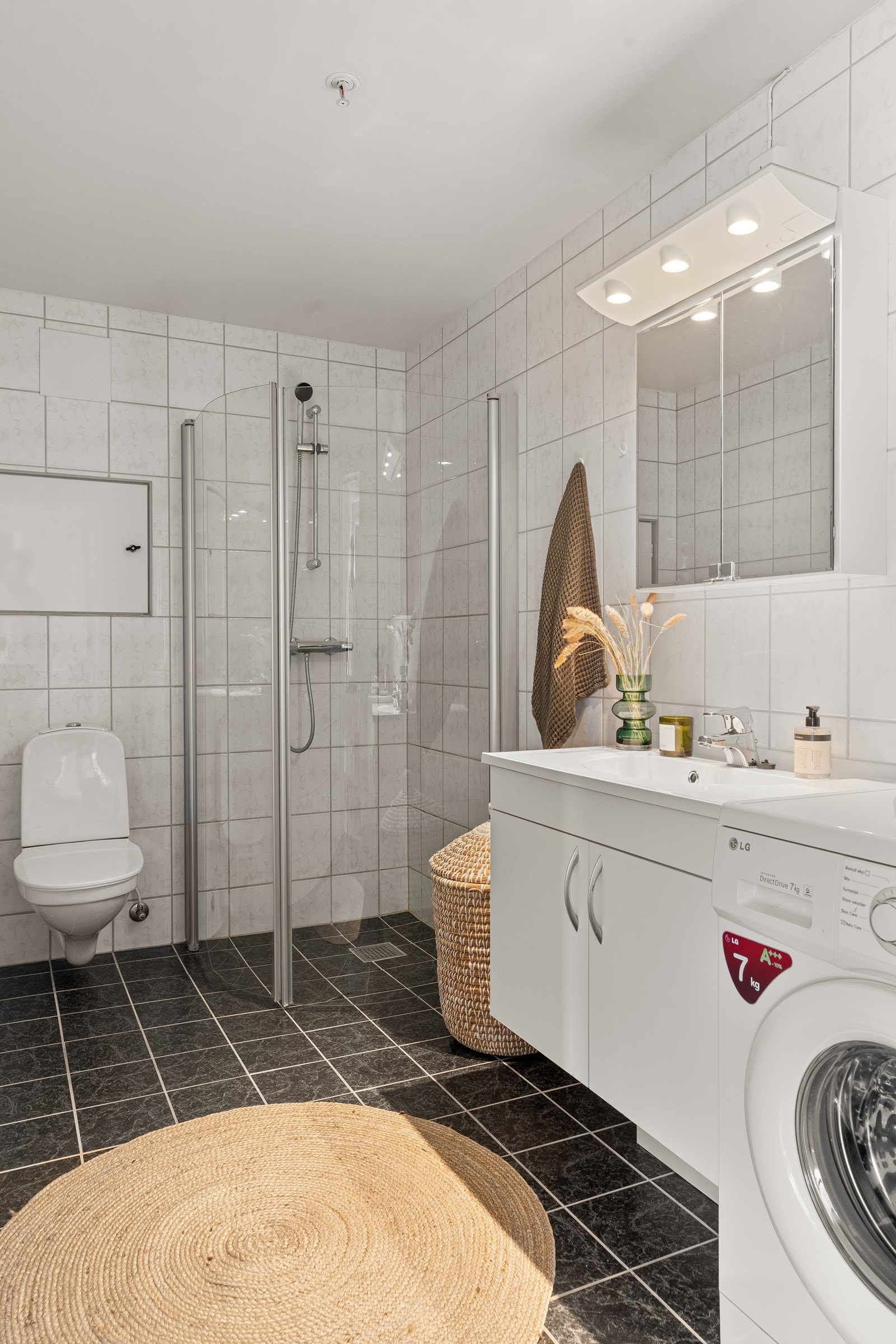 Pent flislagt baderom med gulvvarme, praktisk vegghengt toalett, opplegg for vaskemaskin og dusjhjørne med innfellbare glassdører. Galleribilde