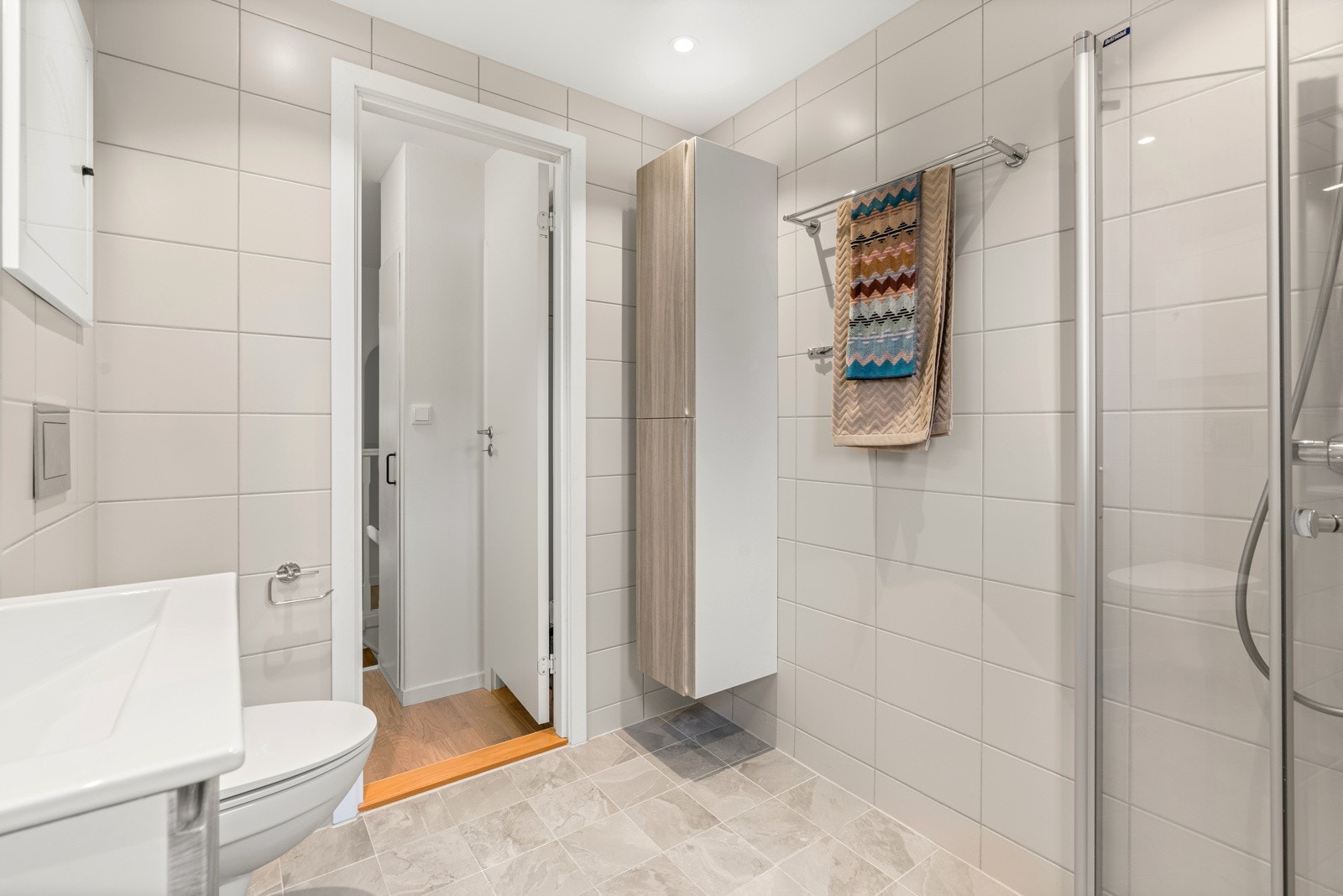 Badet har veggmontert toalett, dusjhjørne med innfellbare fronter og opplegg for vaskemaskin. Galleribilde