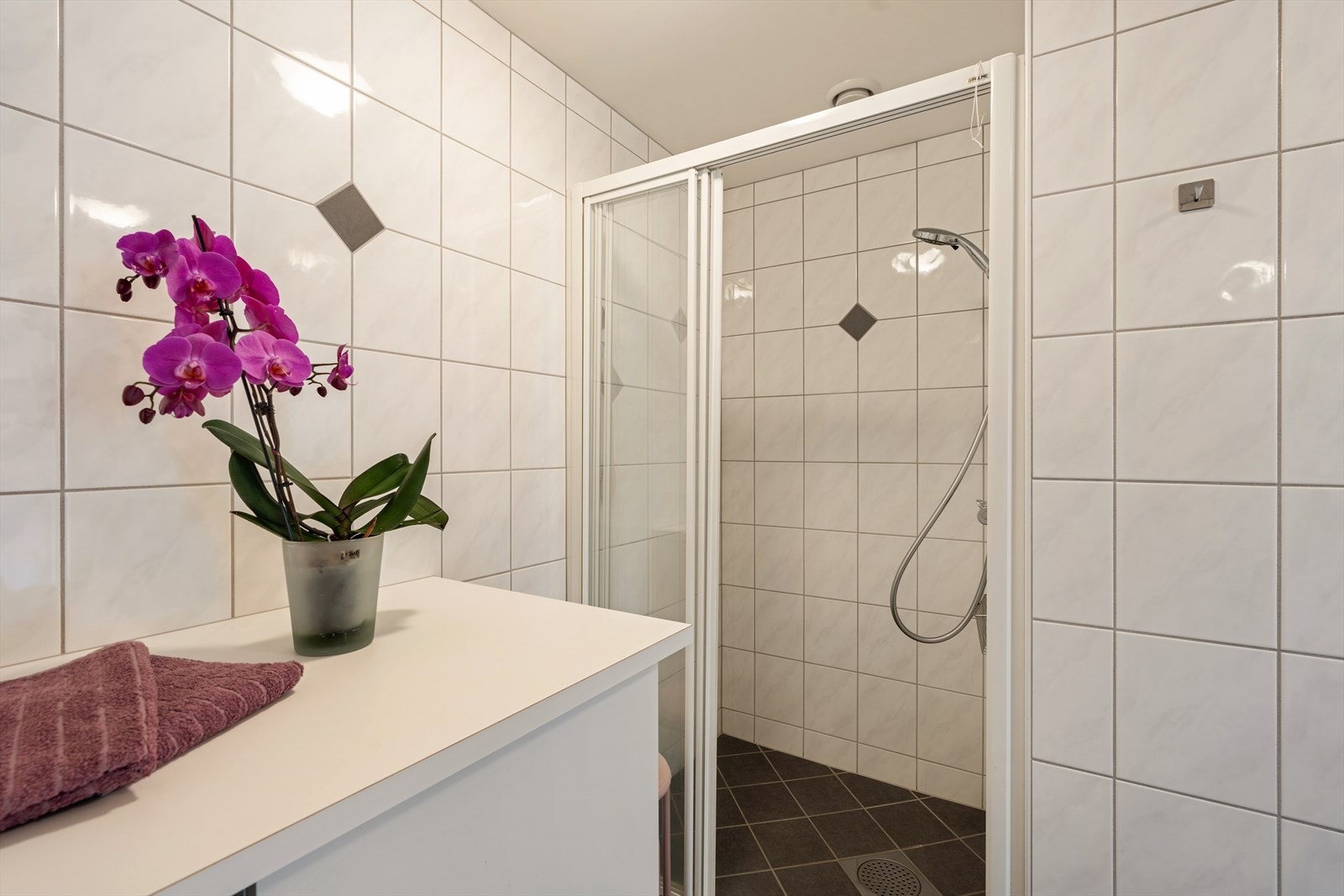 Badet inneholder vegghengt toalett, bide, 2 stk. helstøpte servanter, skuffer under servant med slette fronter, skap over med speilfront, dusjdører i klart glass, opplegg for vaskemaskin og fordelerskap til rørsystemet. Galleribilde