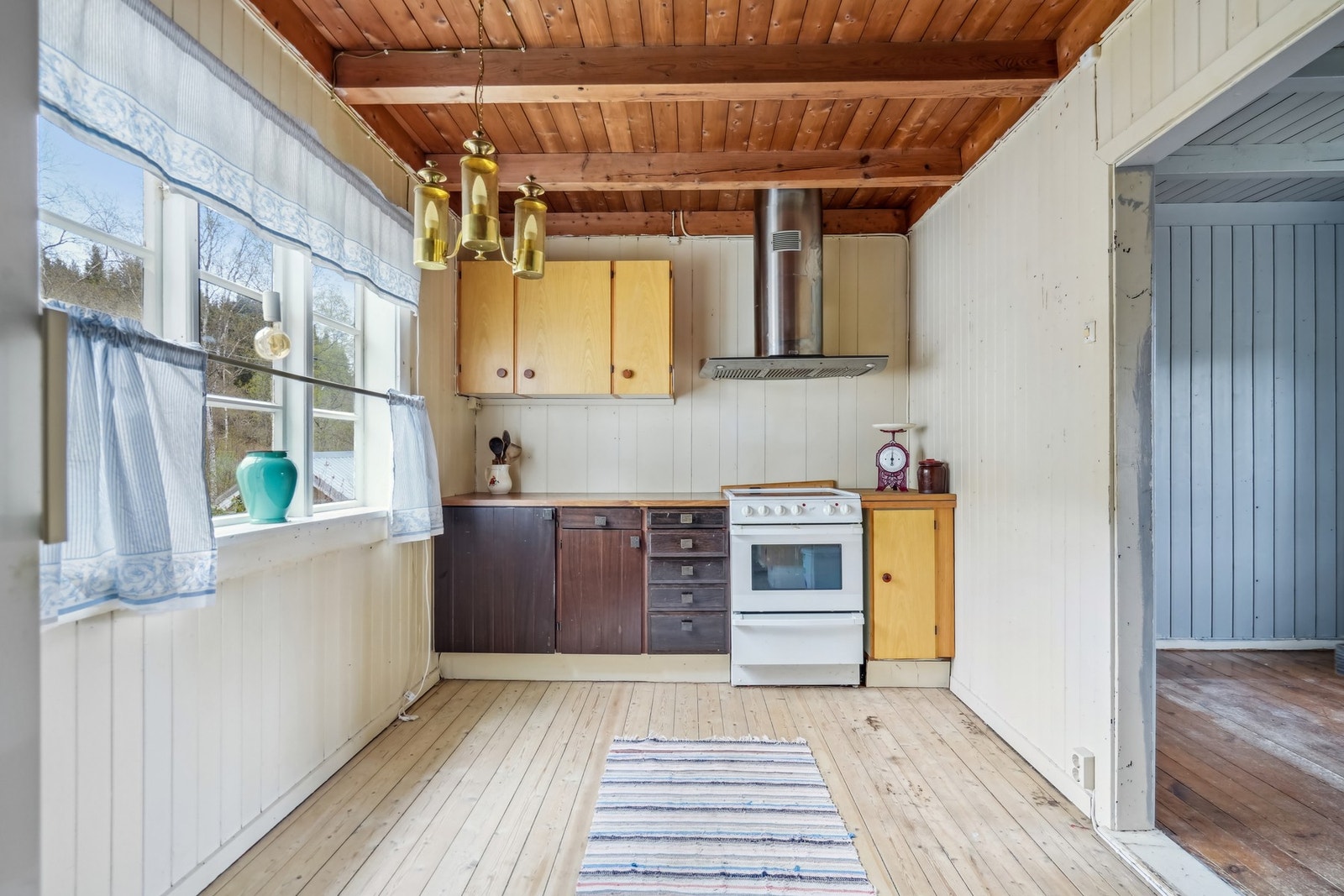 Kjøkken av eldre dato med overskap og underskap, benkeplate av laminat, vask, komfyr og frittstående kjøleskap. Galleribilde