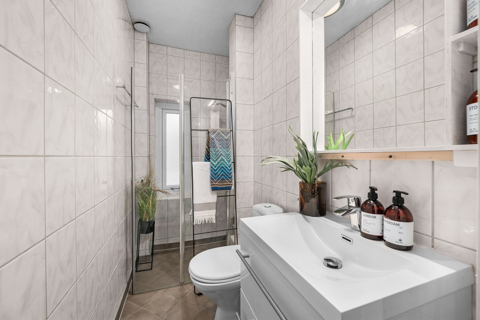 Flislagt bad som består av servantskap med skuffeløsning, speil med hyller, wc, dusjhjørne med glassvegg. Galleribilde