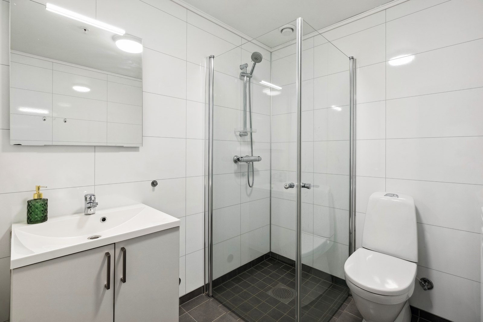 Pent bad med flislagt gulv og baderomsplater på veggene. Galleribilde