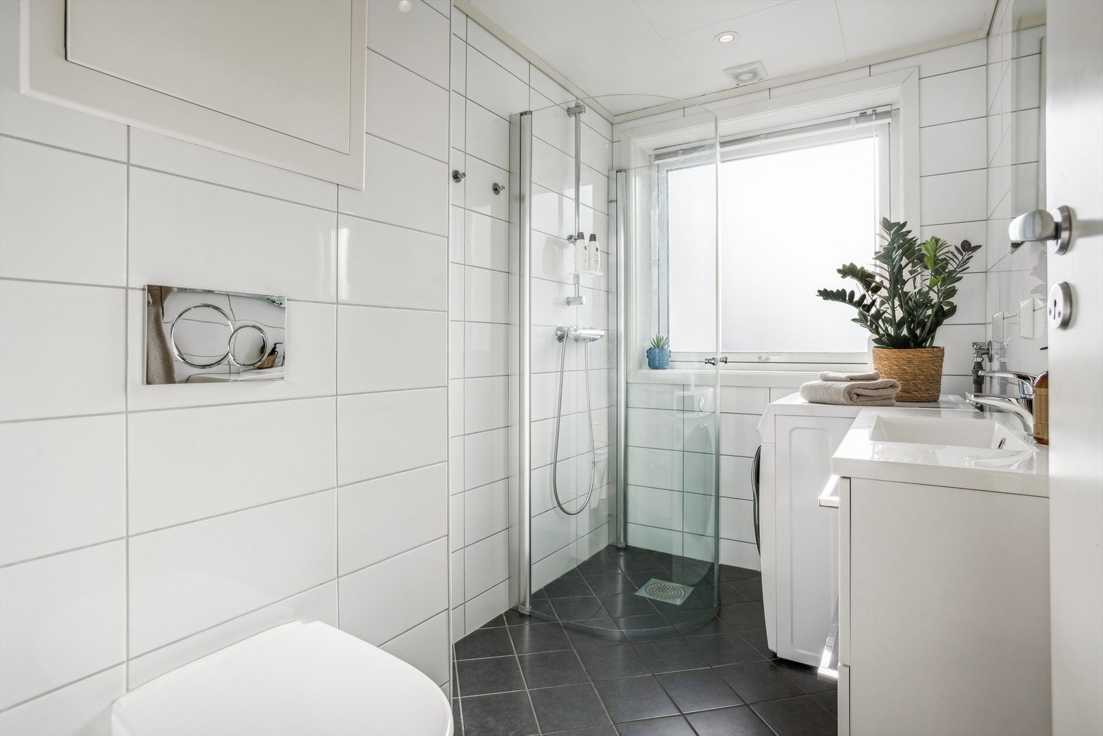 Rommet har fliser på gulv og vegger og inneholder dusj, opplegg for vaskemaskin, servant med innredning og vegghengt toalett. Galleribilde