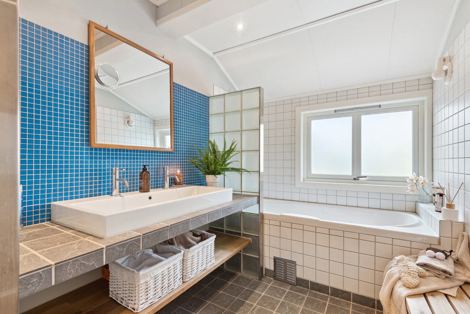 Ett av to bad i hovedetasjen. Rommet har fliser på gulvet, vegger med fliser og malt strie. Badet er innredet med servant i plassbygd og flislagt benkeinnredning, innfliset badekar med vegghengt armatur, speil og vegghengt toalett. Galleribilde