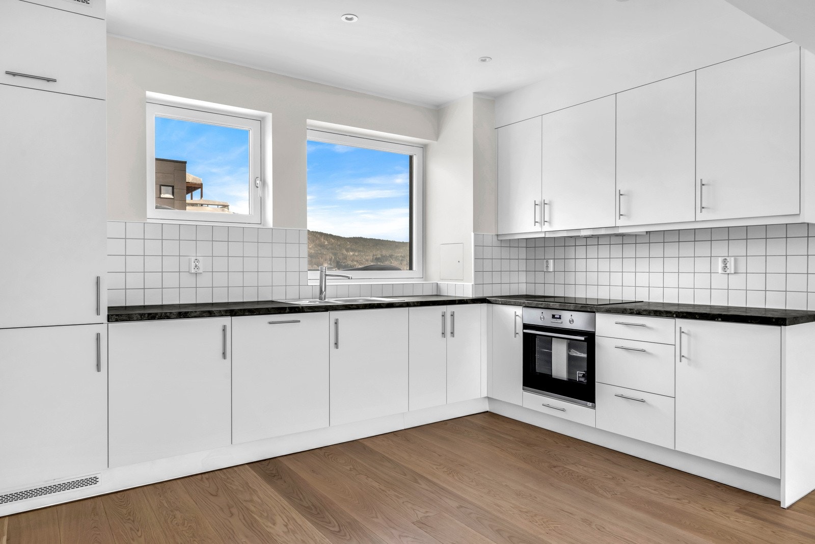 Kjøkkenet er utstyrt med moderne og elegante hvite fronter og en rustfri stålkum som gir kjøkkenet et strømlinjeformet utseende. Integrerte hvitevarer fra anerkjente leverandøren AEG gir deg det praktiske du trenger. Galleribilde