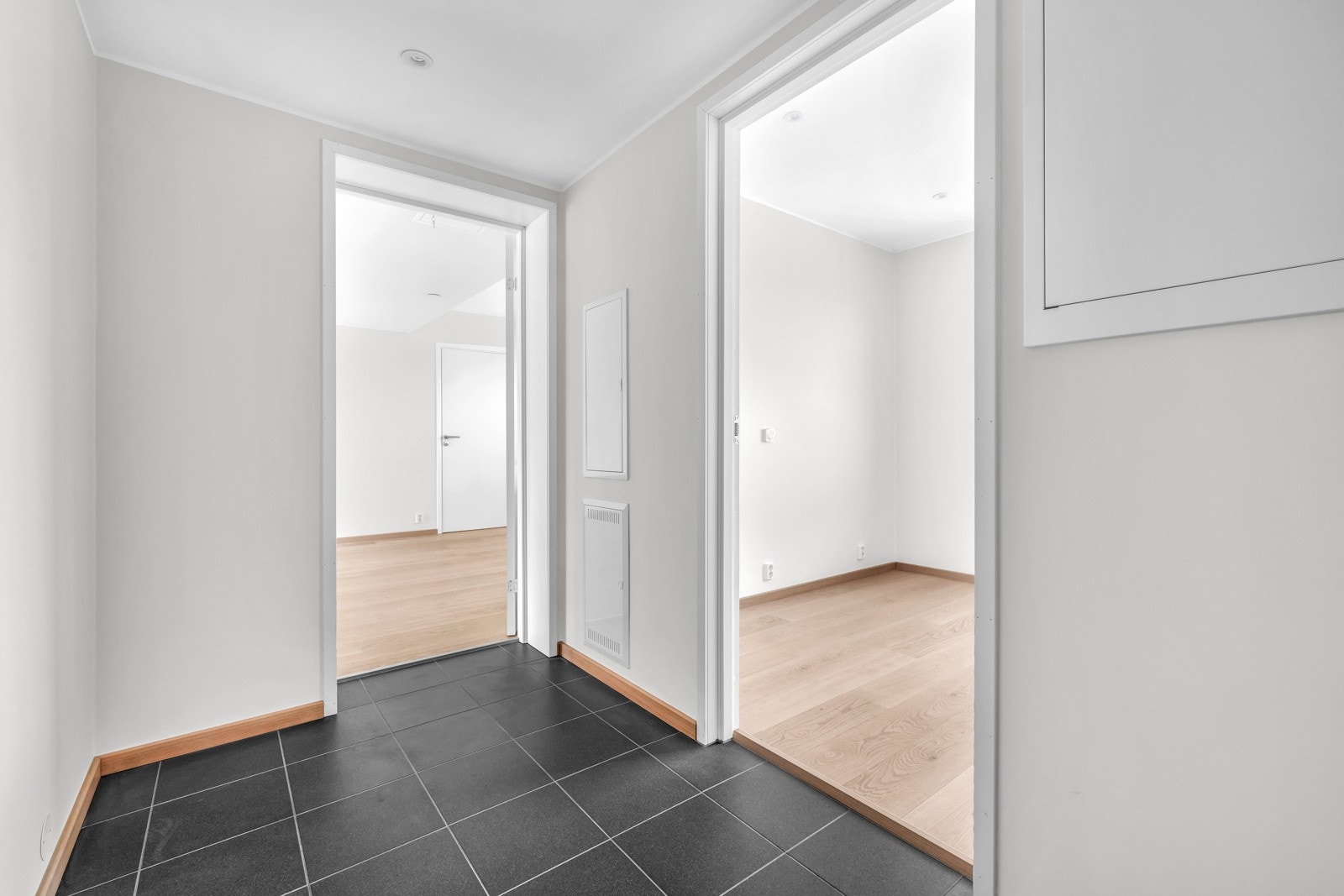 Den romslige entréen er en invitasjon til å utforske resten av boligen, en inngangsport til komfort, eleganse og funksjonalitet. Her smelter varmen i gulvet sammen med estetikken i flisene for å skape en vakker velkomst. Galleribilde