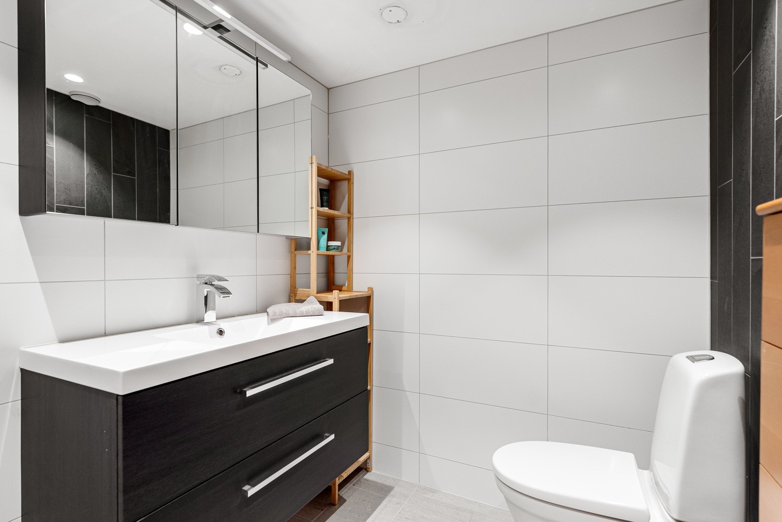 Badet er innredet med toalett, innfellbart dusjhørne og servant med møblement, speilskap og beysning. Galleribilde