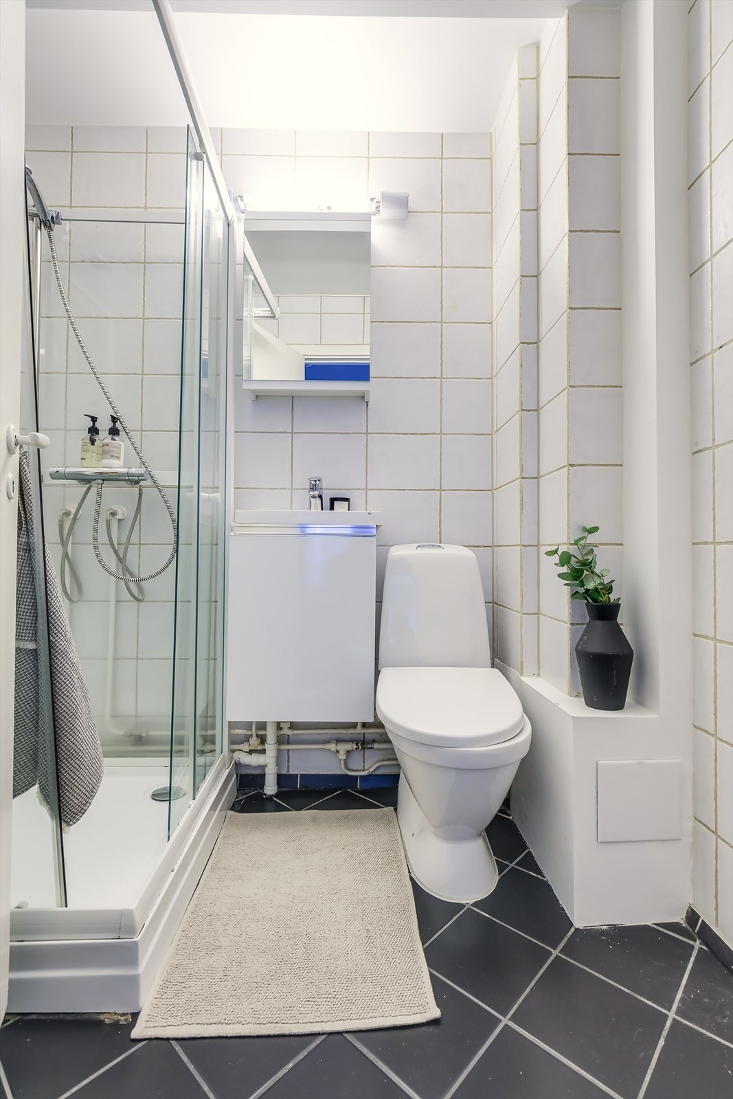 Flislagt baderom med dusjkabinett, servant skapseksjon og overskap for oppbevaring Galleribilde