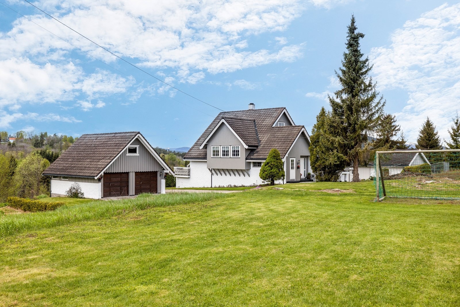 Stor gårdsplass med belegningsstein og dobbel garasje med lader til el-bil. Galleribilde