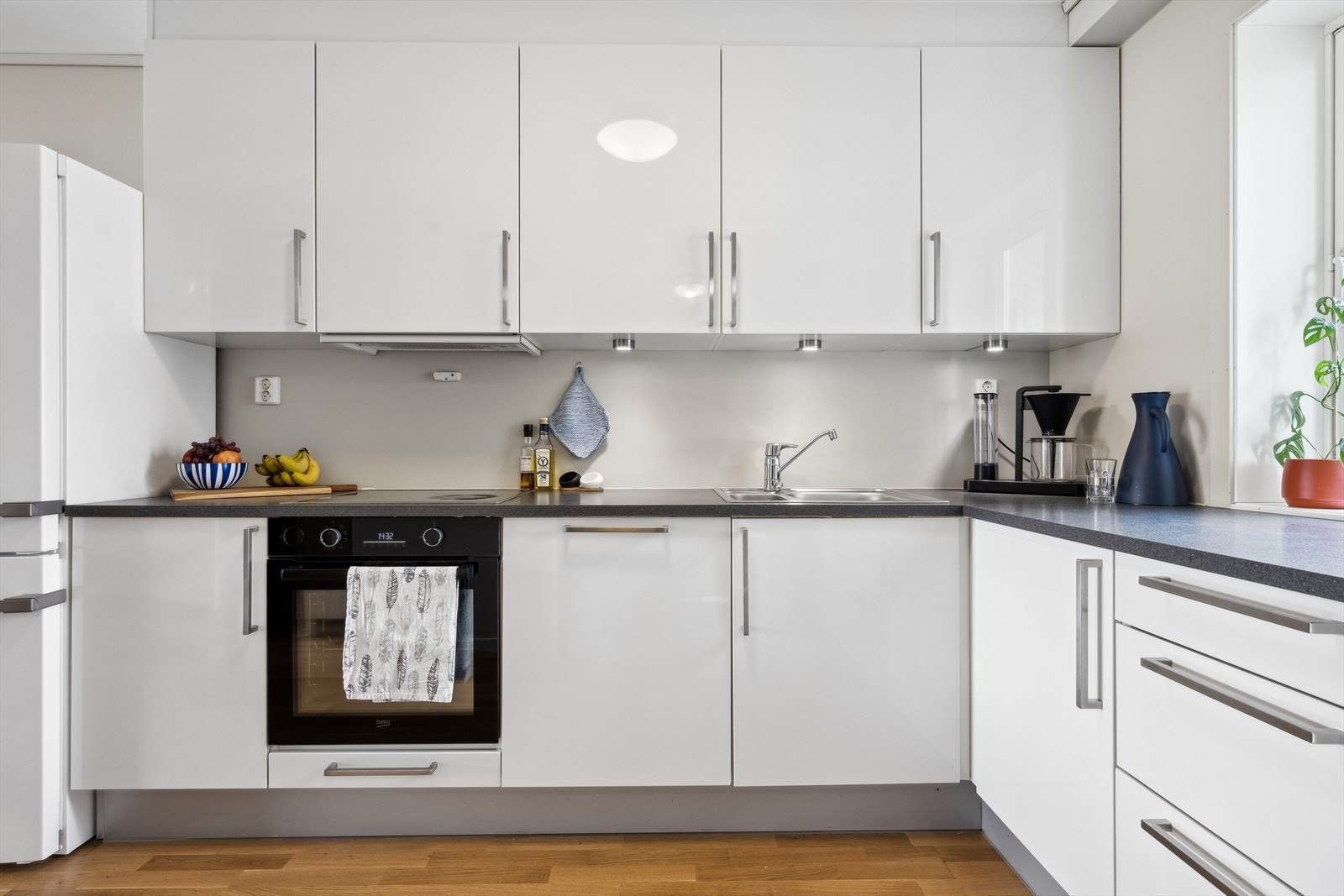 Pent kjøkkeninnredning med glatte hvite fronter med laminert benkeplate. Galleribilde